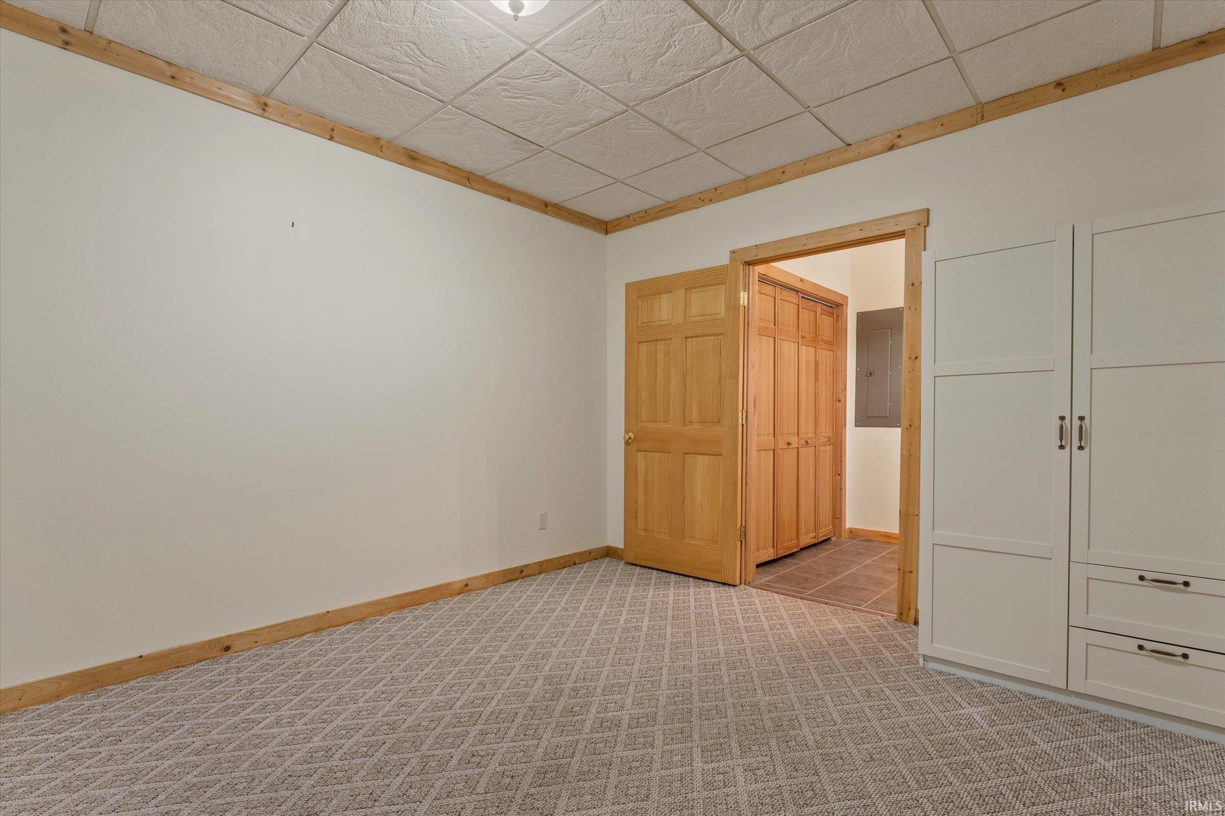 Unfurnished bedroom with light colored carpet, a drop ceiling, and electric panel