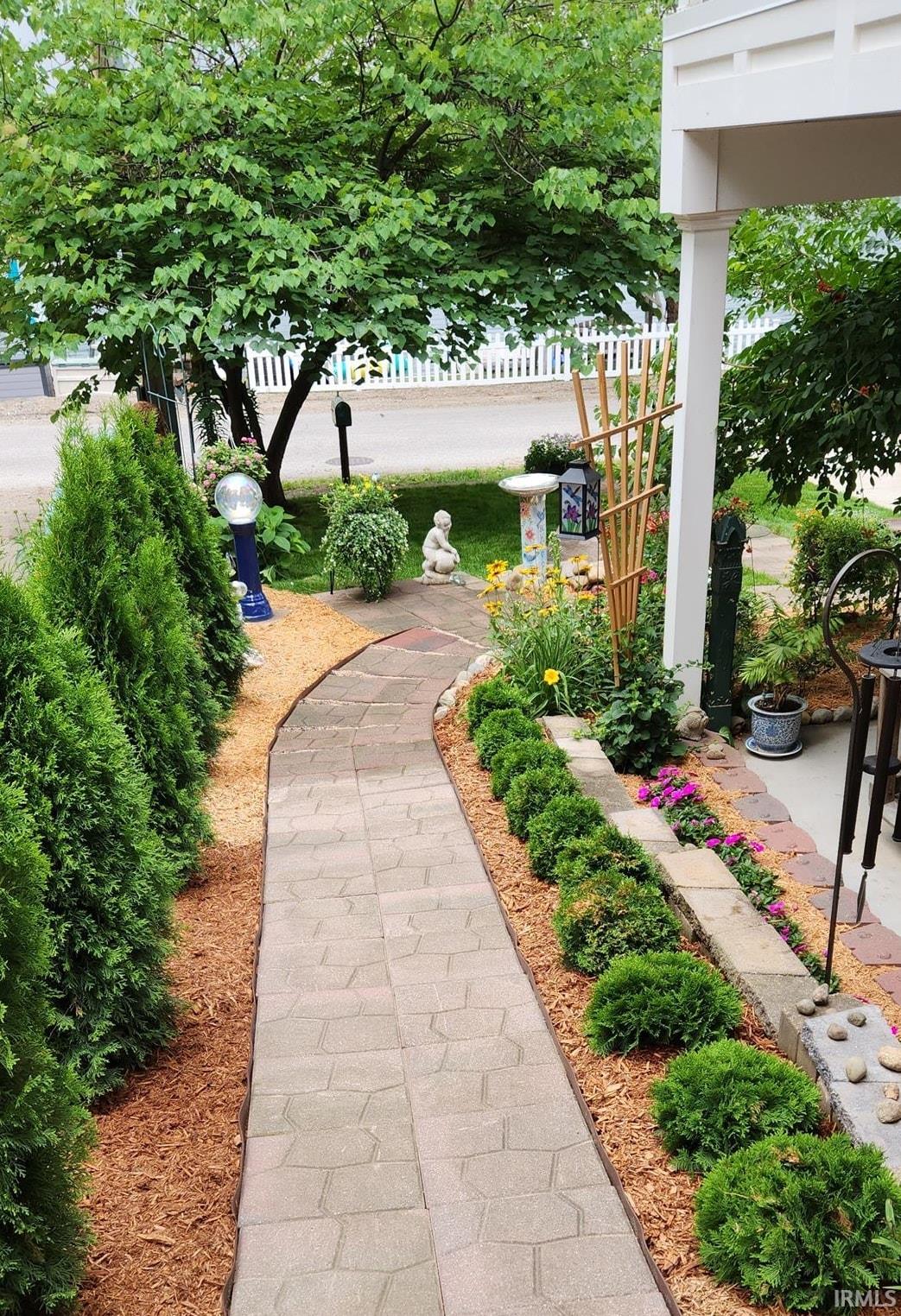 Curved paver pathway bordered by mature evergreen shrubs and manicured landscaping