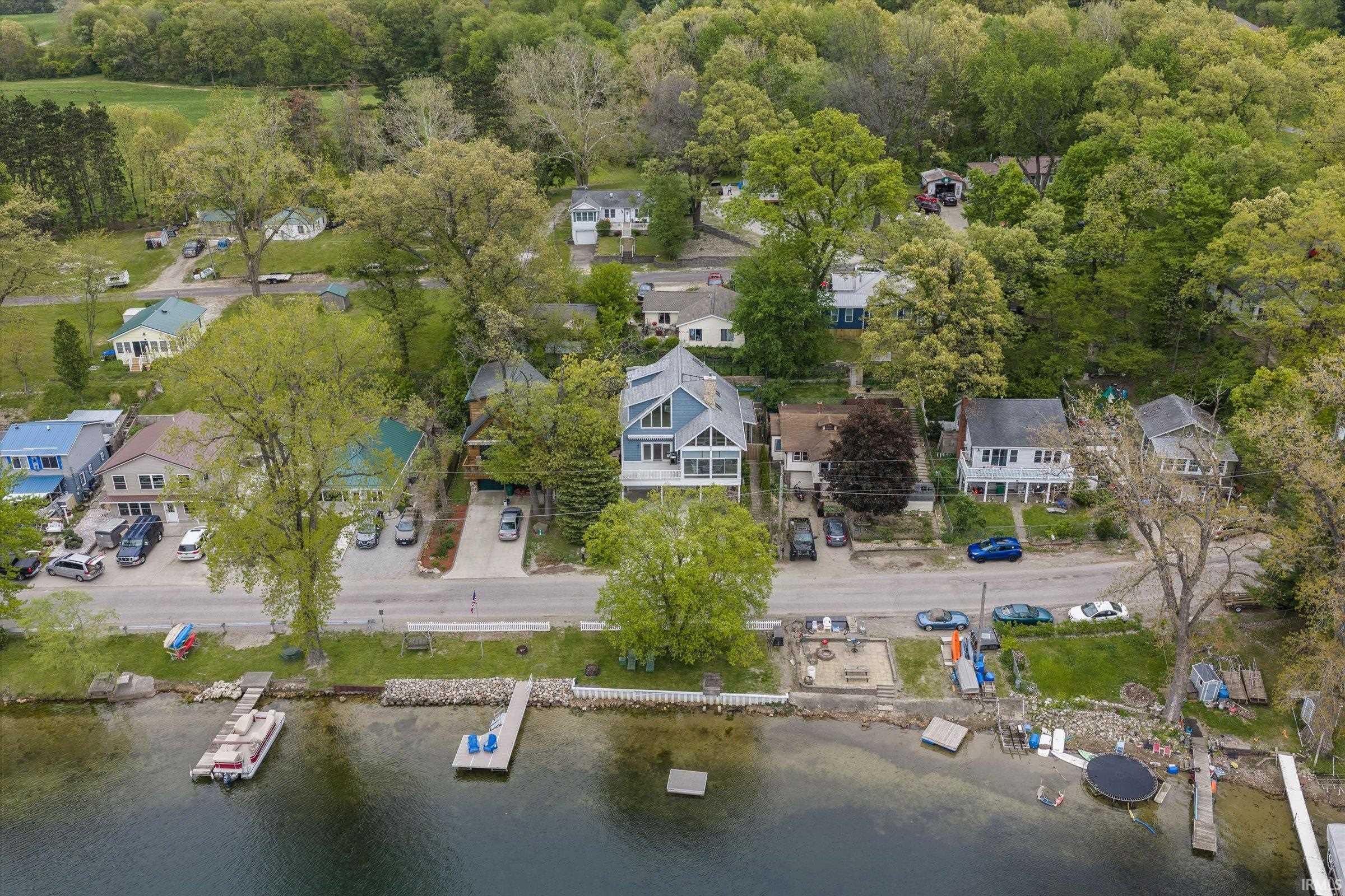 Waterfront property featuring a private dock, direct lake access, a gravel parking area, and mature trees surrounding the home