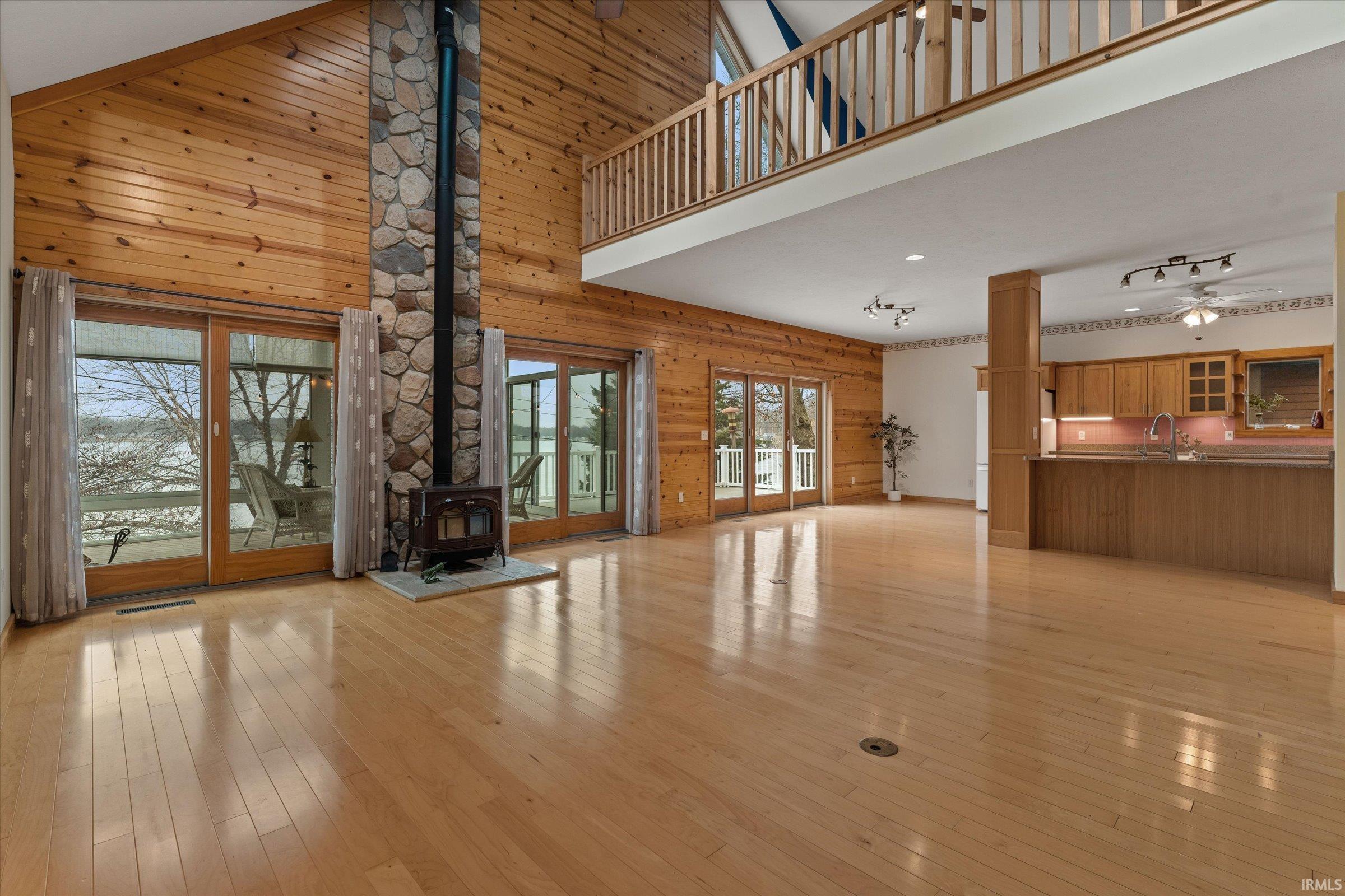 Unfurnished living room featuring wood walls, a high ceiling, a ceiling fan, light wood finished floors, and a wood stove