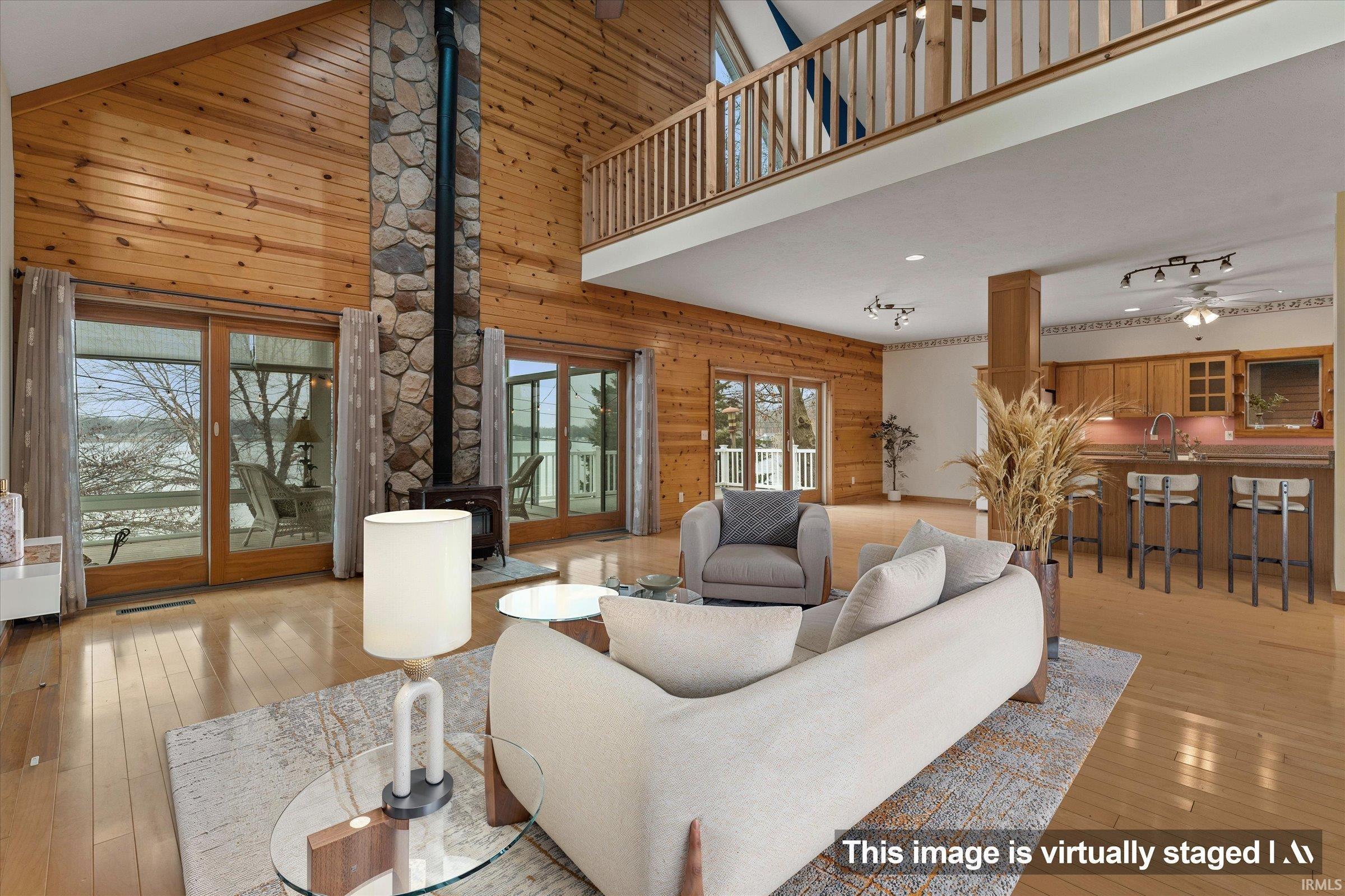 Living room featuring wood walls, a high ceiling, a wood stove, a ceiling fan, and light wood-style flooring