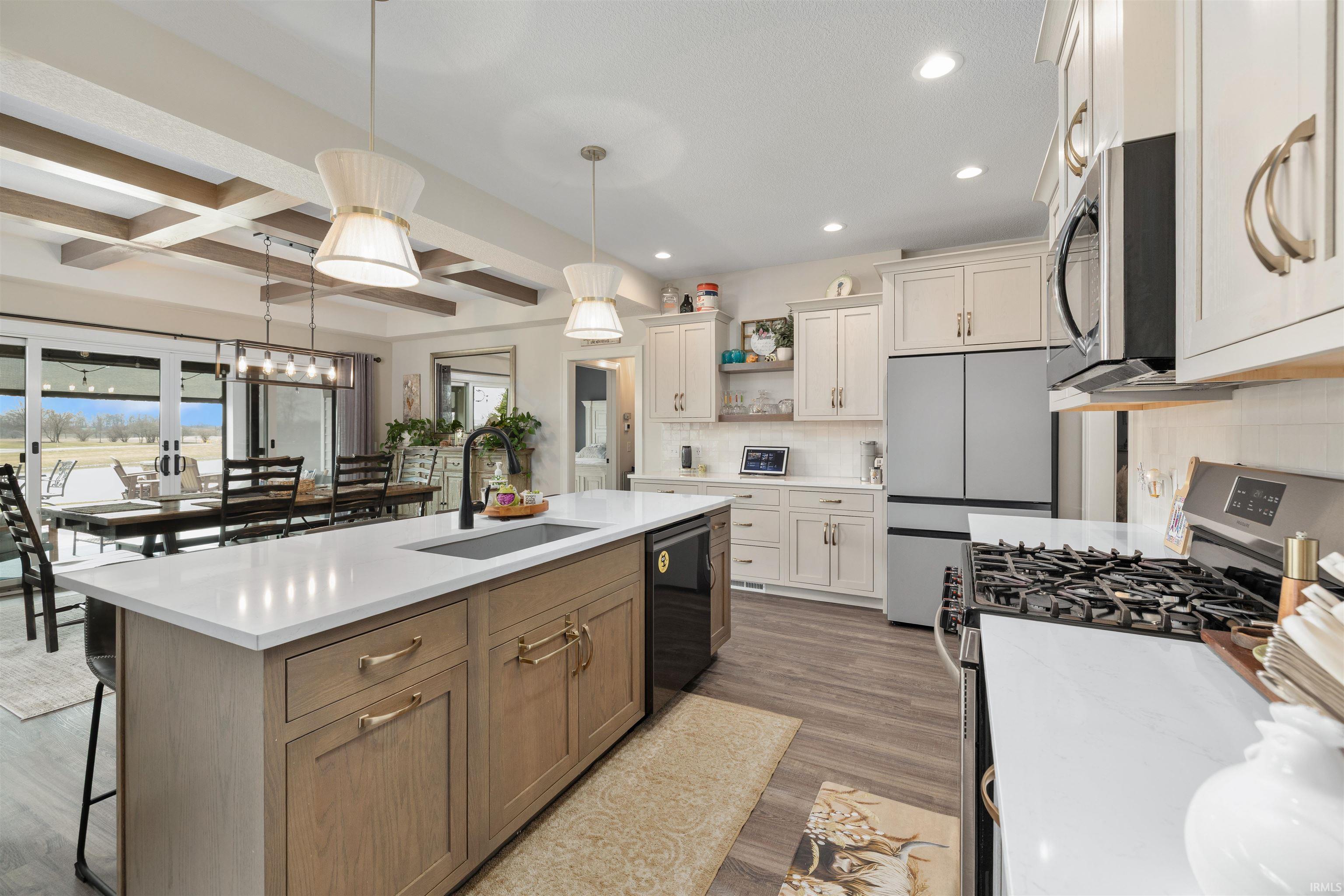 Kitchen featuring stainless steel appliances, two tone cabinetry, an island with sink, decorative backsplash, and pendant lighting