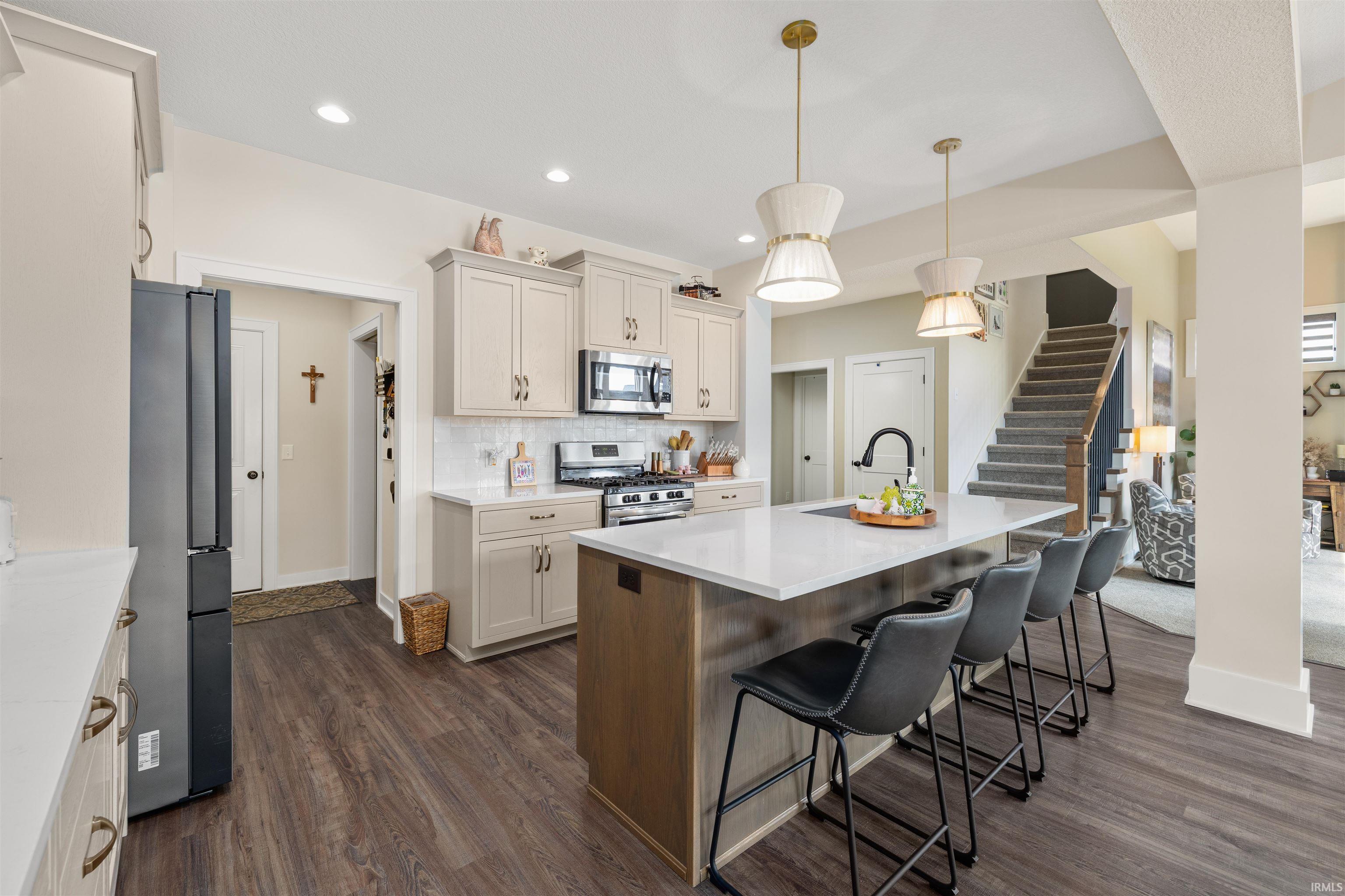 Dual tone kitchen with a kitchen bar, stainless steel appliances, a center island with sink, two tone color scheme, and dark wood-style flooring