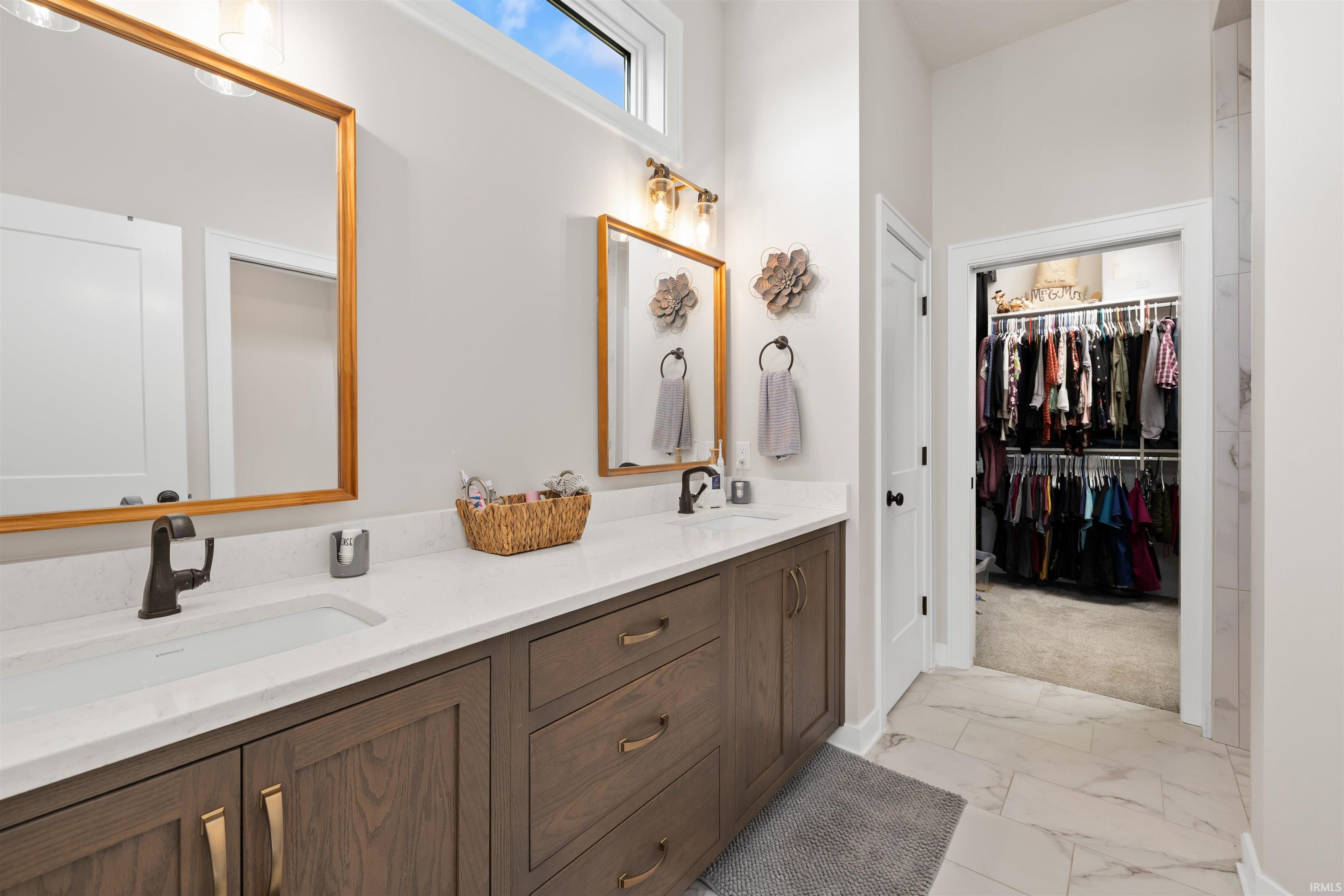 Bathroom featuring double vanity, a walk in closet, and light marble finish floors