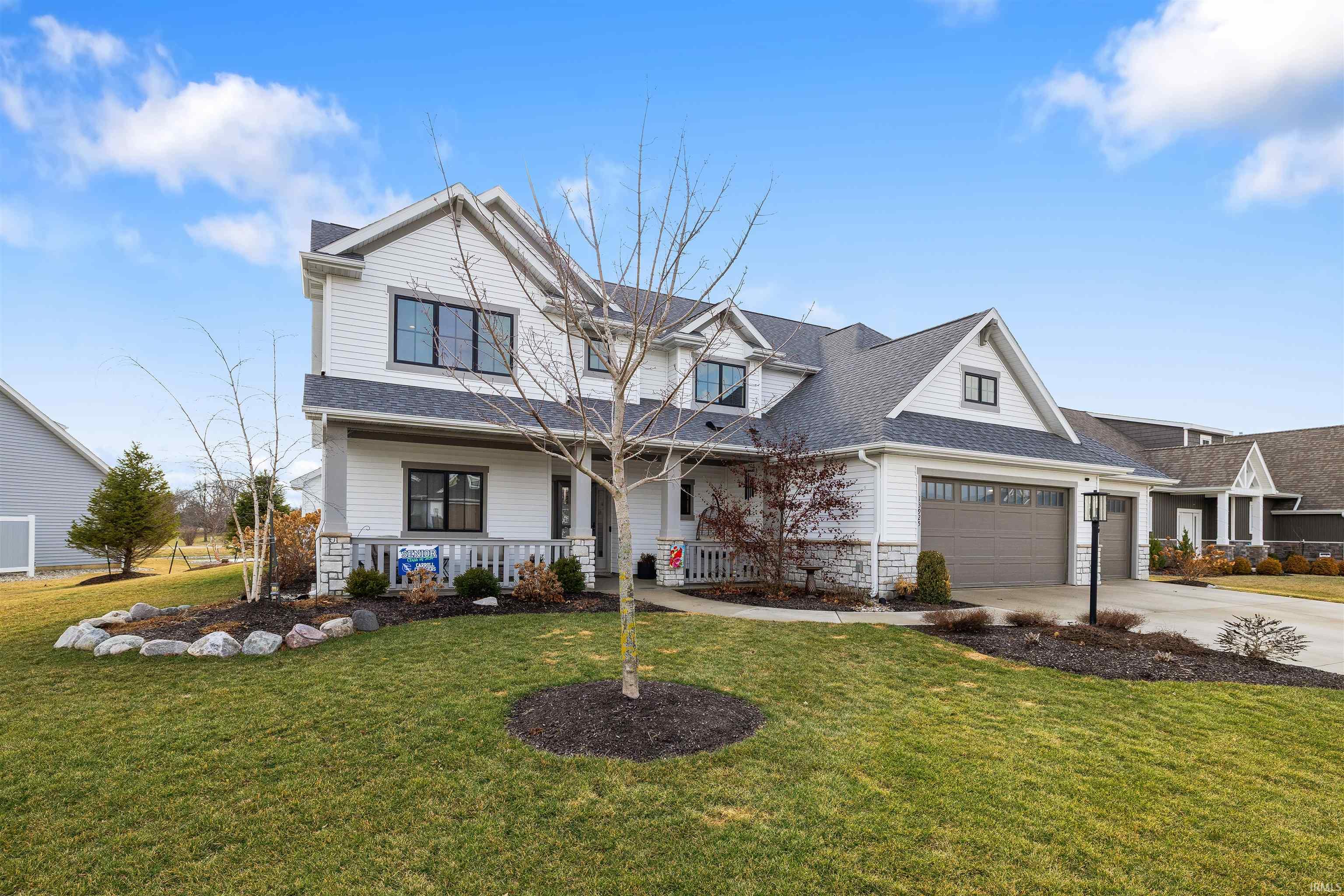 View of front of property featuring covered porch, driveway, a front lawn, and an attached garage