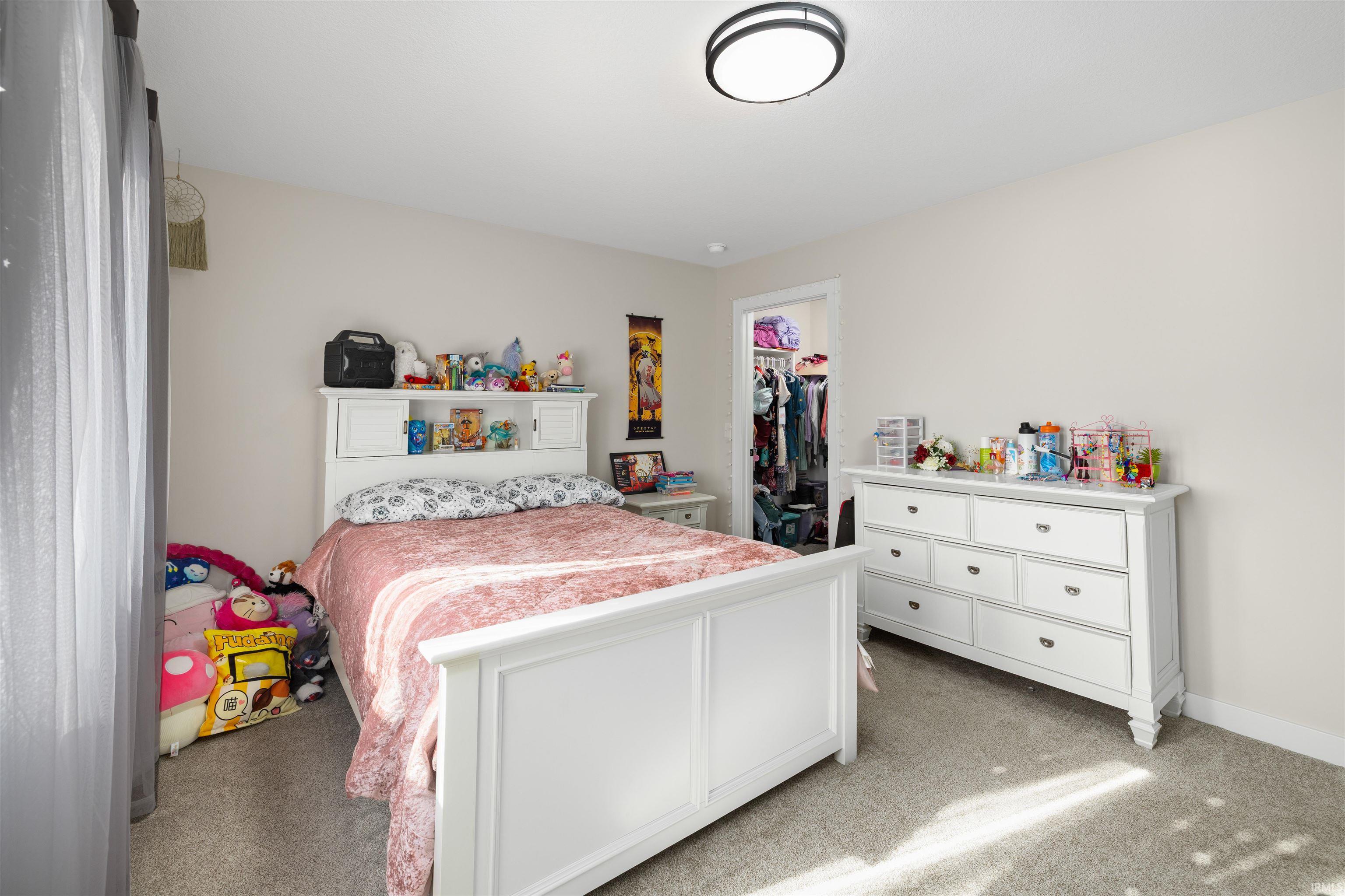 Bedroom with light colored carpet and a walk in closet