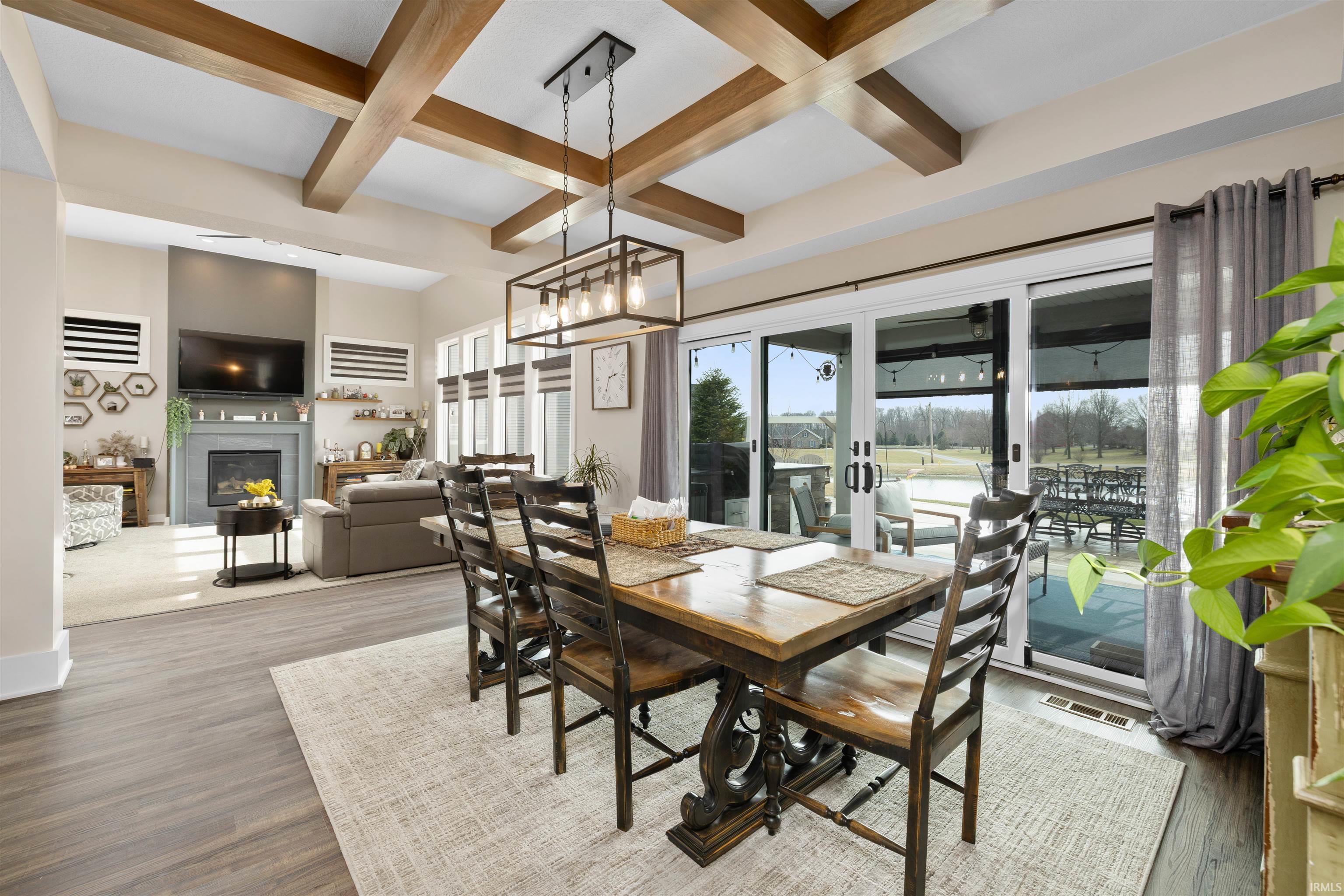 Dining space with coffered ceiling, a glass covered fireplace, wood finished floors, and hanging lights