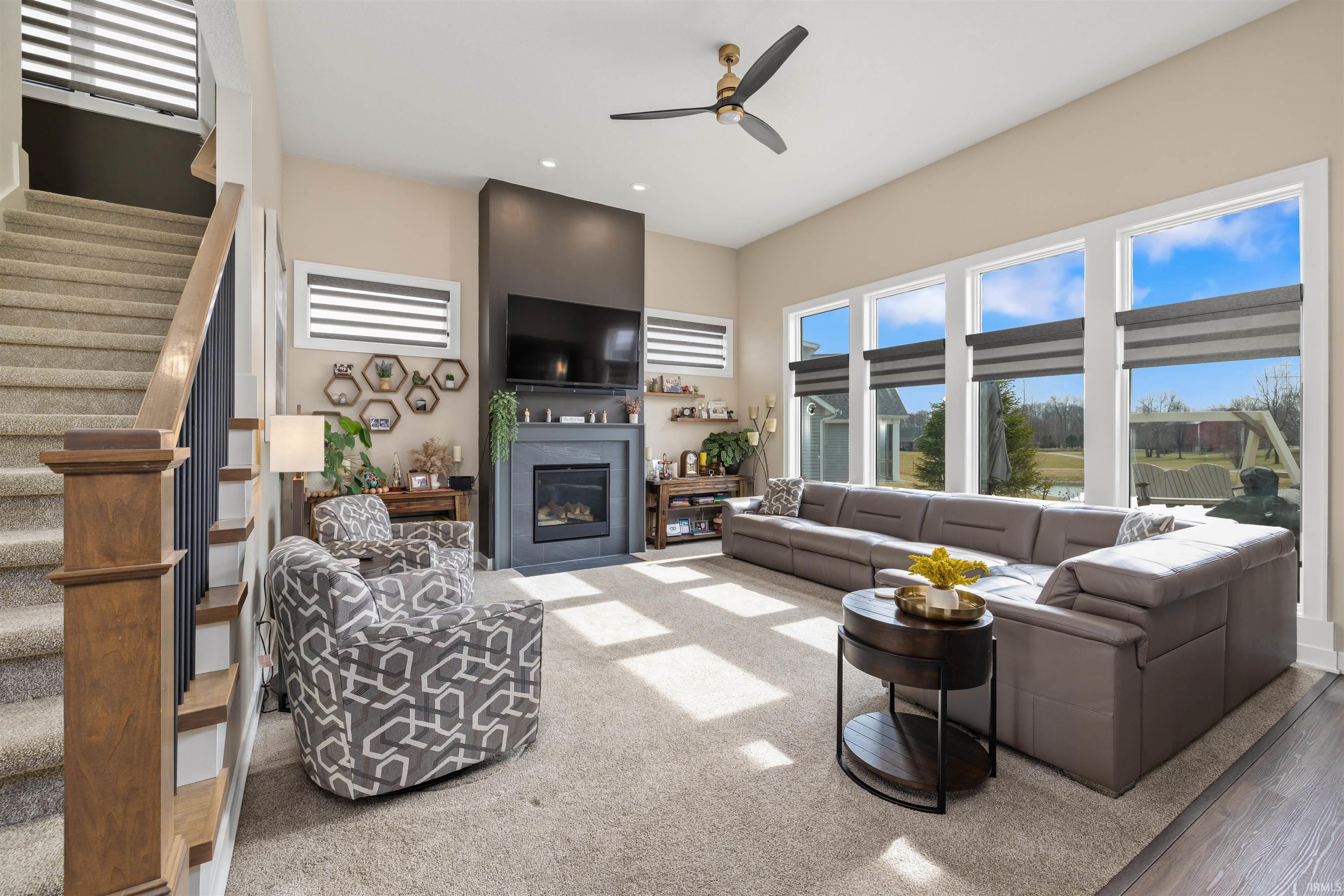 Living area with ceiling fan, a glass covered fireplace, recessed lighting, and a high ceiling