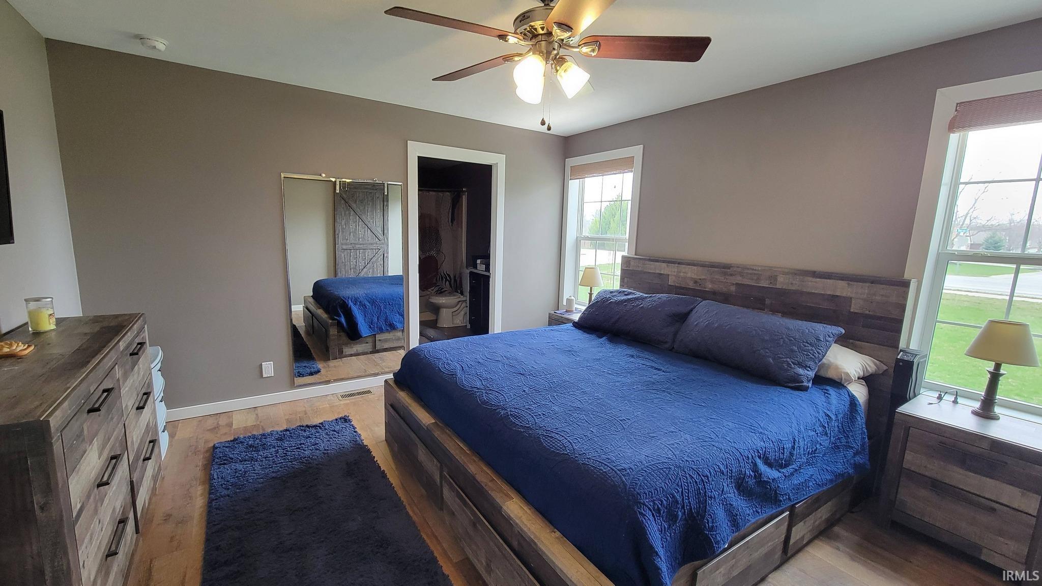 Bedroom with light wood-style floors, a ceiling fan, and ensuite bath