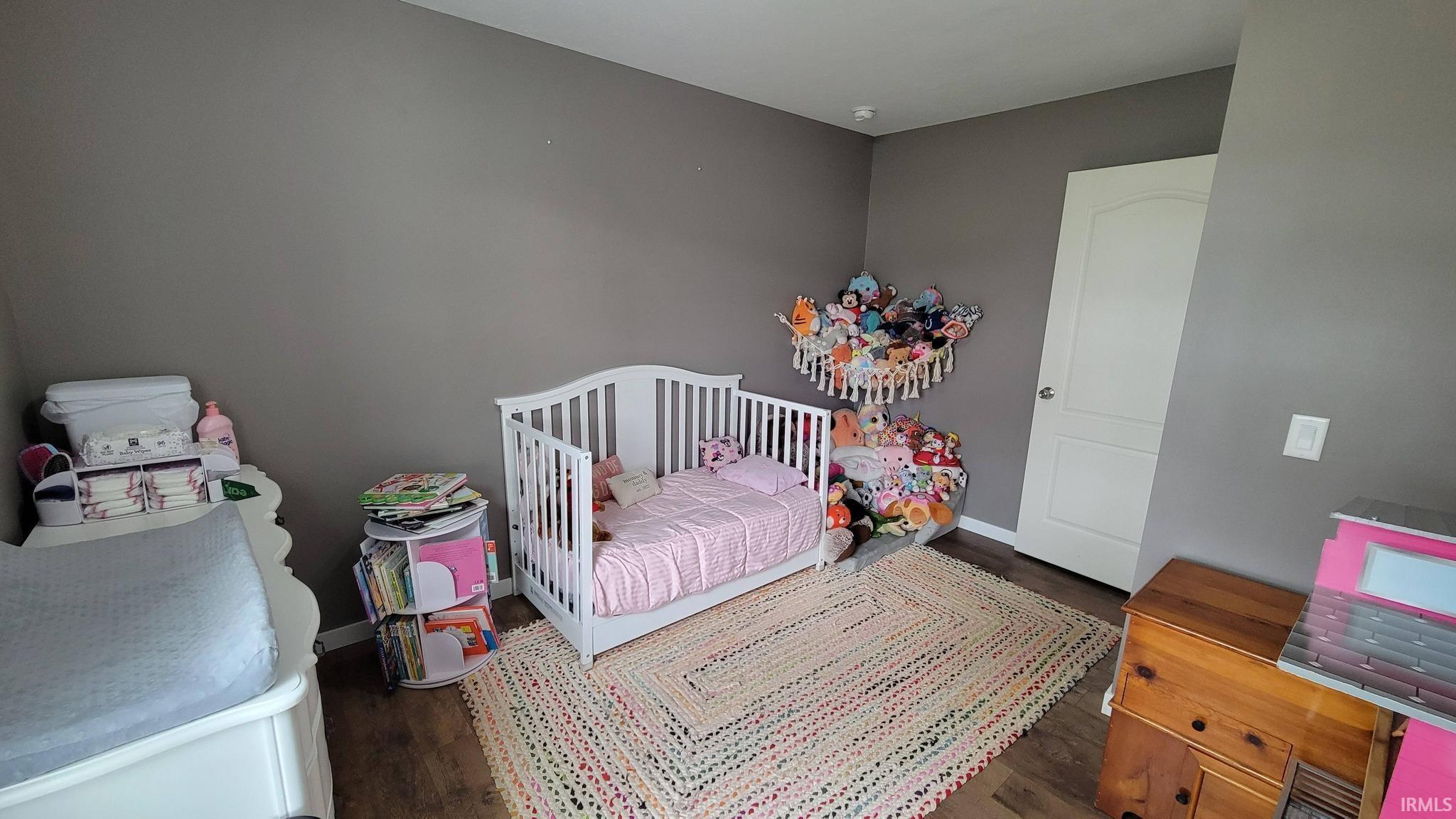 Bedroom featuring a nursery area and dark wood-type flooring