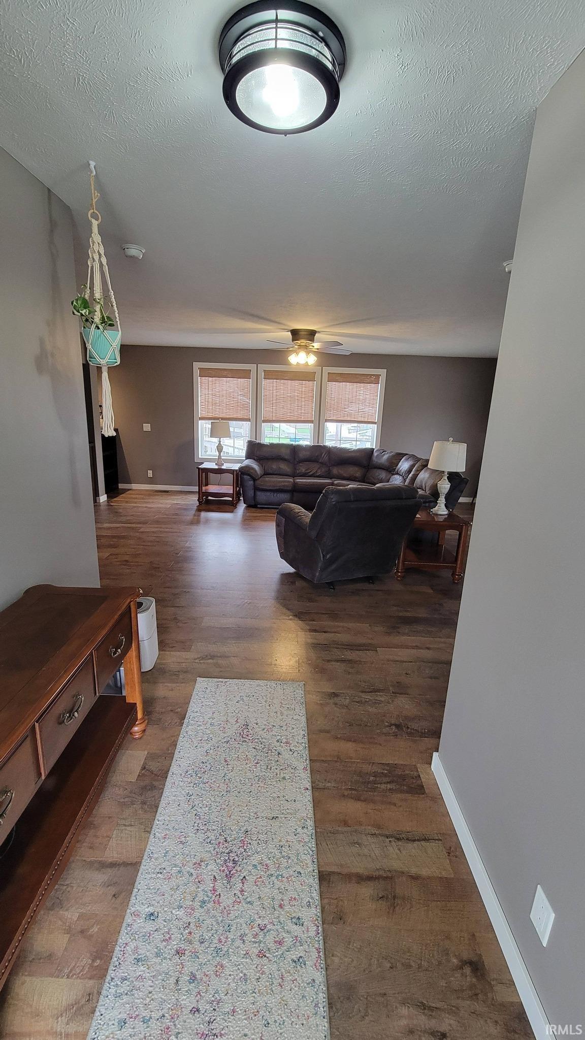 Living room with dark wood-style floors, a textured ceiling, and a ceiling fan