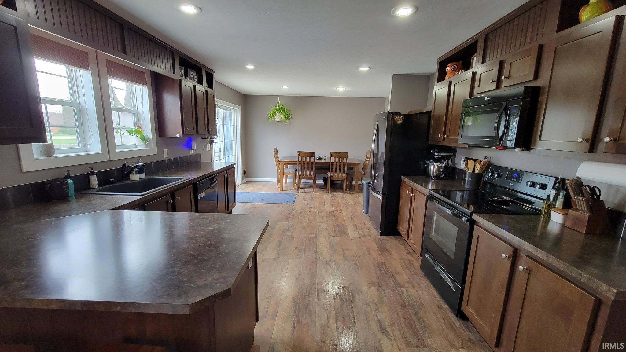 Kitchen featuring black appliances, dark countertops, dark wood finish cabinetry, open shelves, and light wood-style flooring