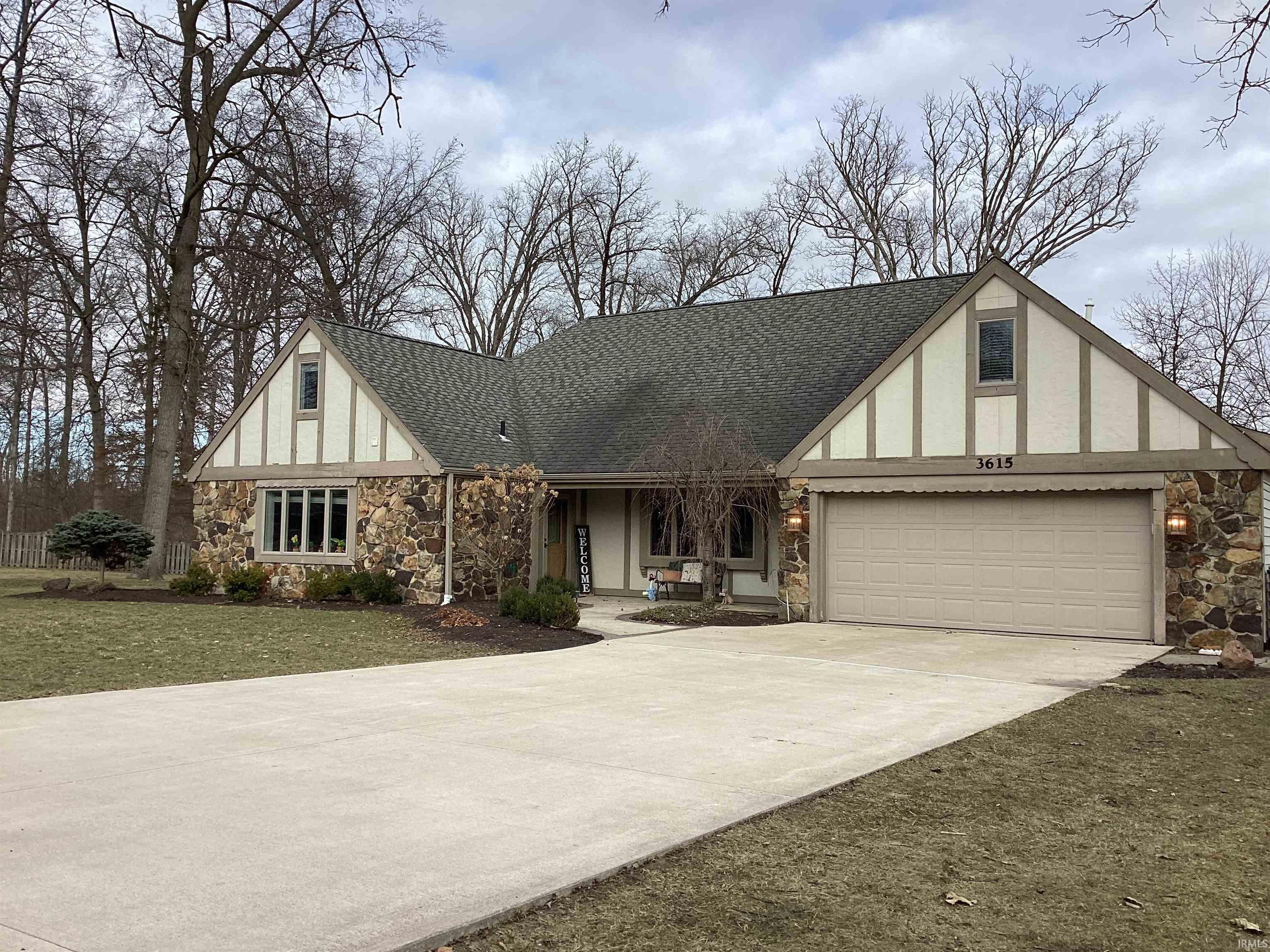 Tudor house with stone siding, a porch, a shingled roof, driveway, and a front yard