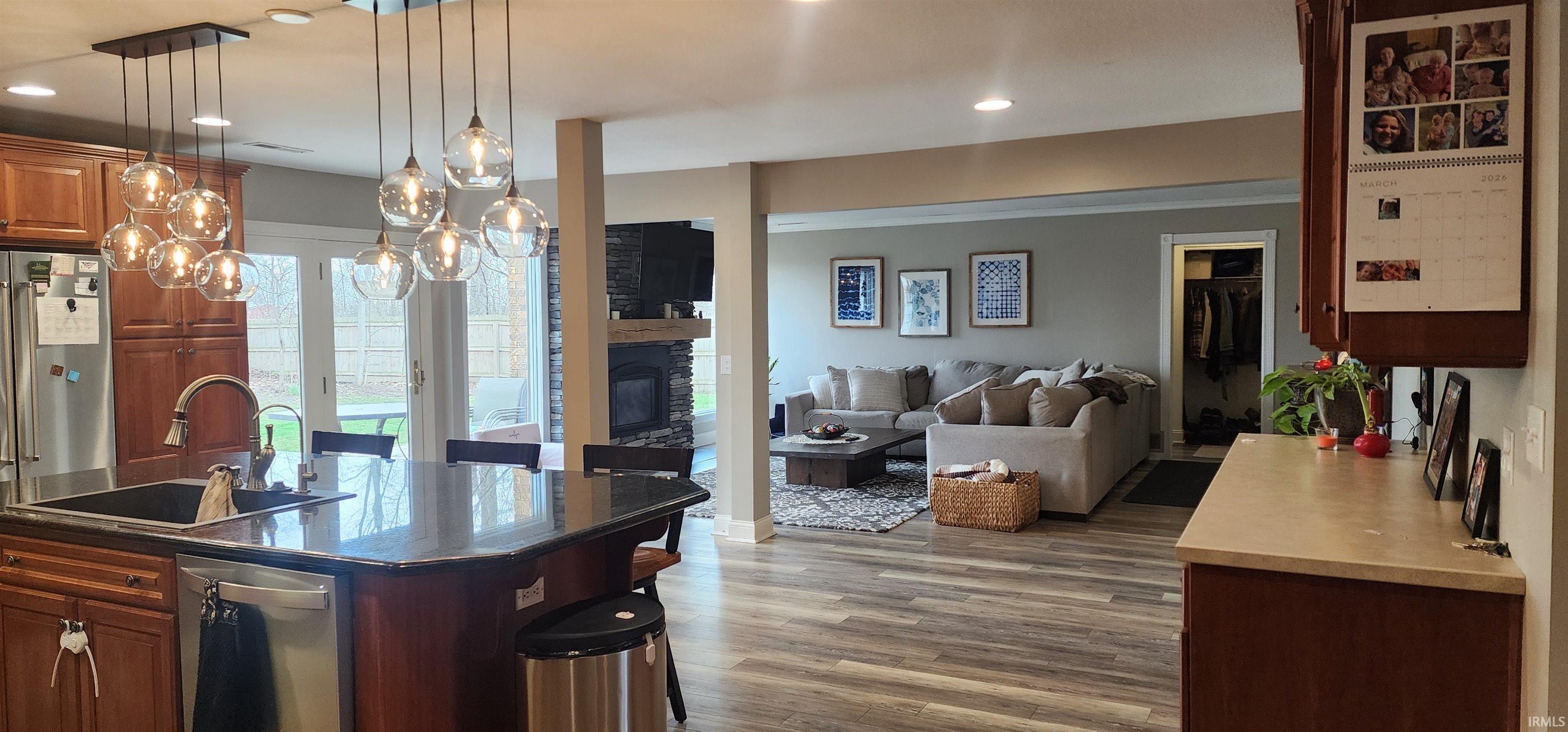 Kitchen featuring open floor plan, a glass covered fireplace, stainless steel dishwasher, light wood-style floors, and a kitchen breakfast bar