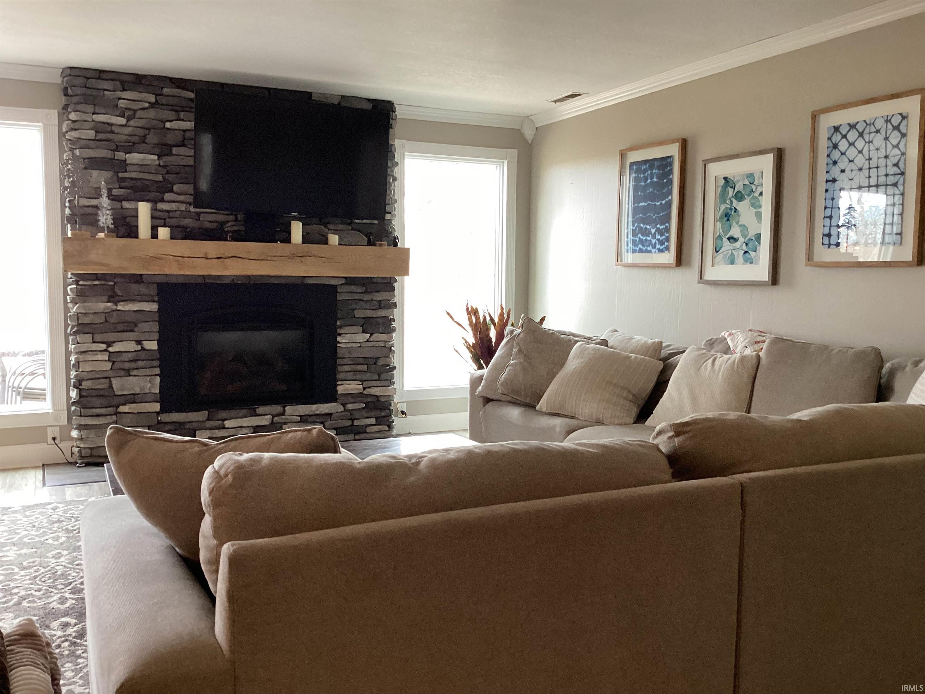 Living area featuring ornamental molding and a stone fireplace