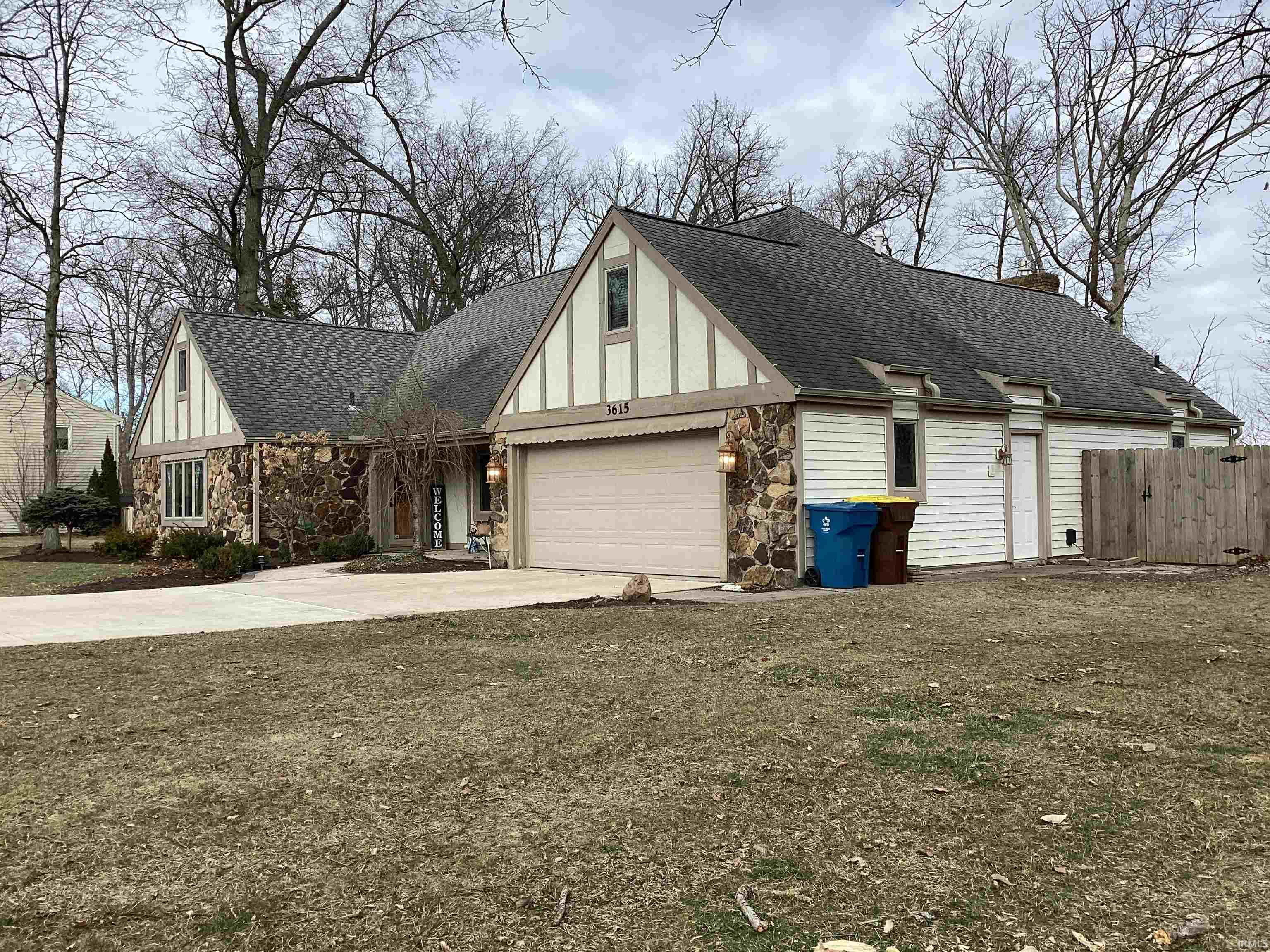 View of front of home featuring roof with shingles, concrete driveway, stone siding, and a chimney