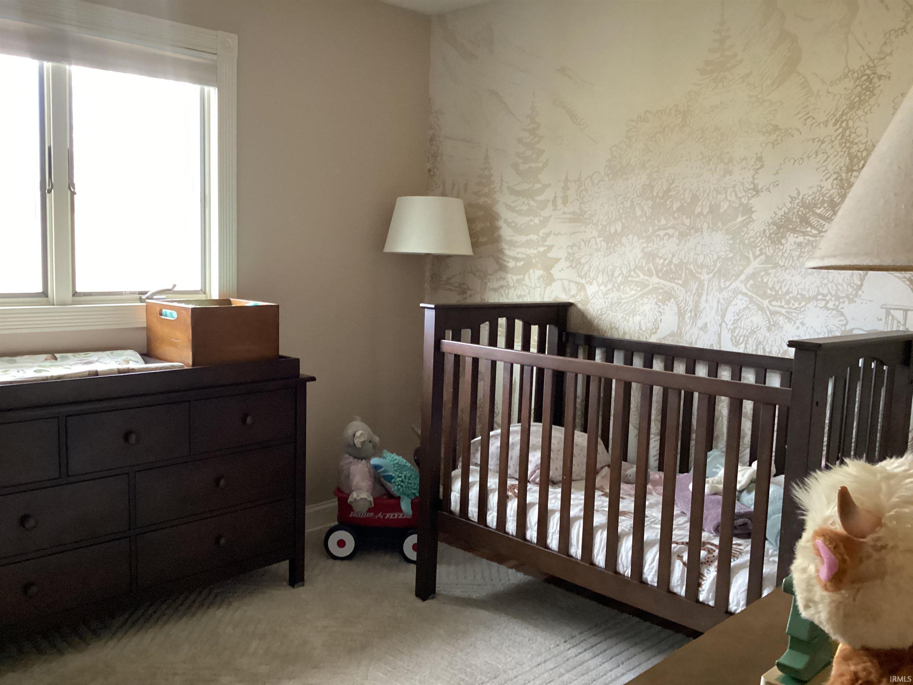 Bedroom with a crib, light colored carpet, and wallpapered walls