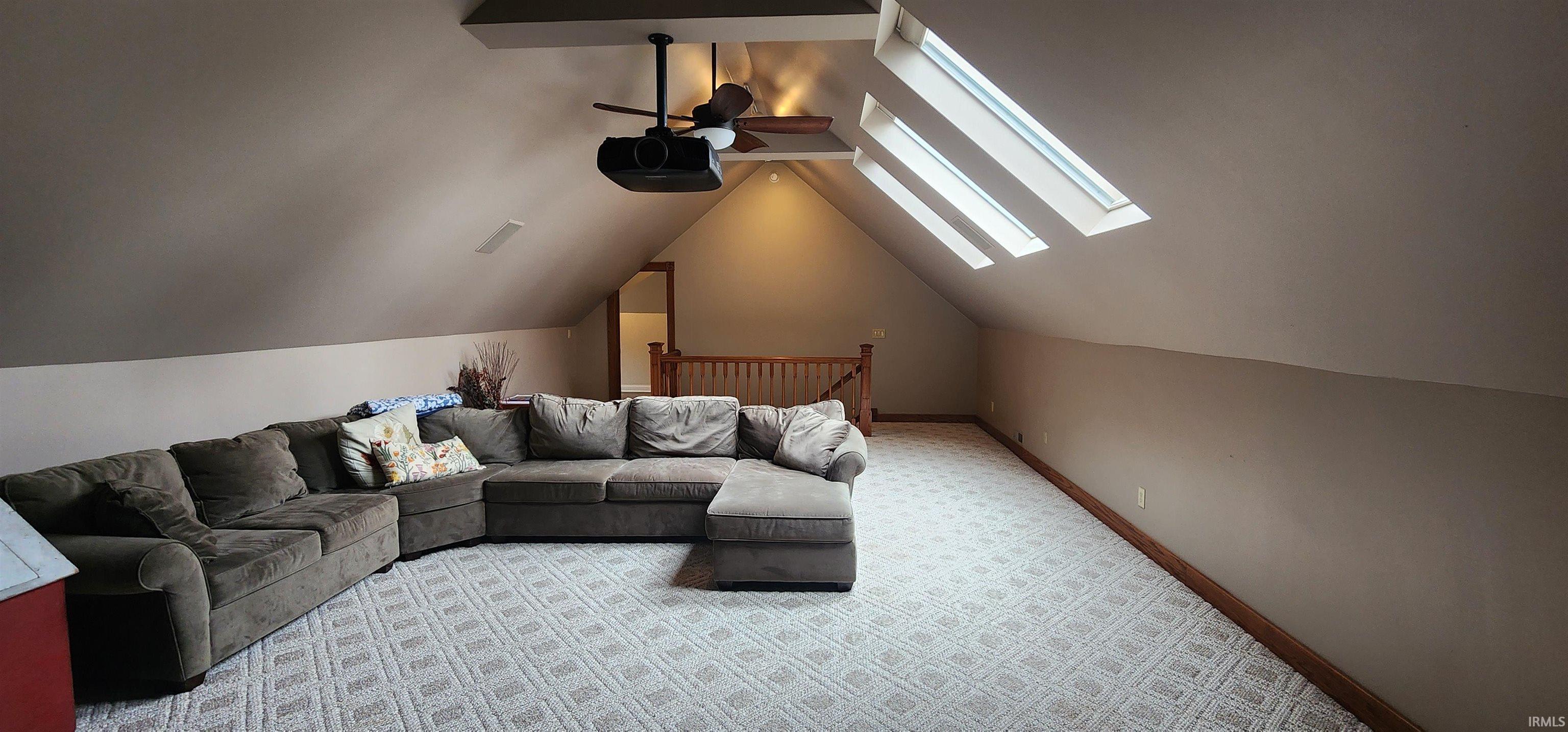 Living room with a ceiling fan, a skylight, light colored carpet, and vaulted ceiling