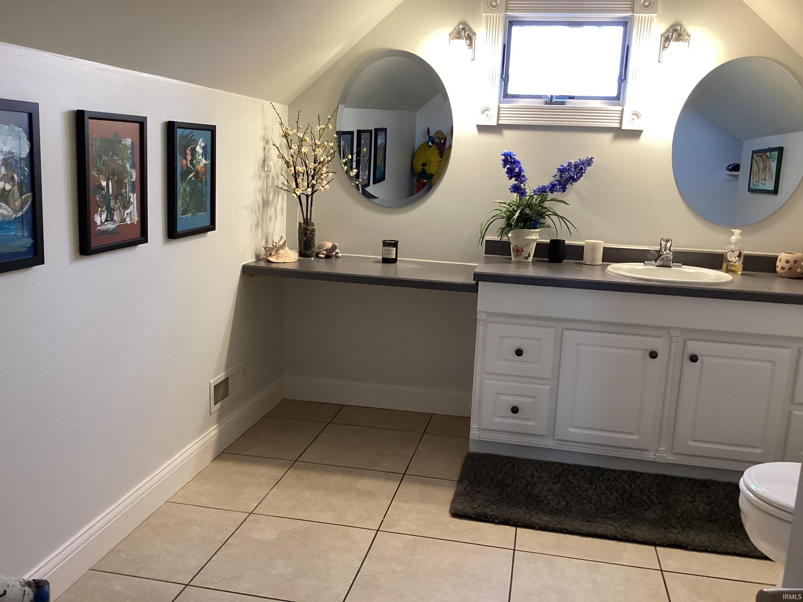 Bathroom featuring vanity, light tile patterned flooring, and lofted ceiling