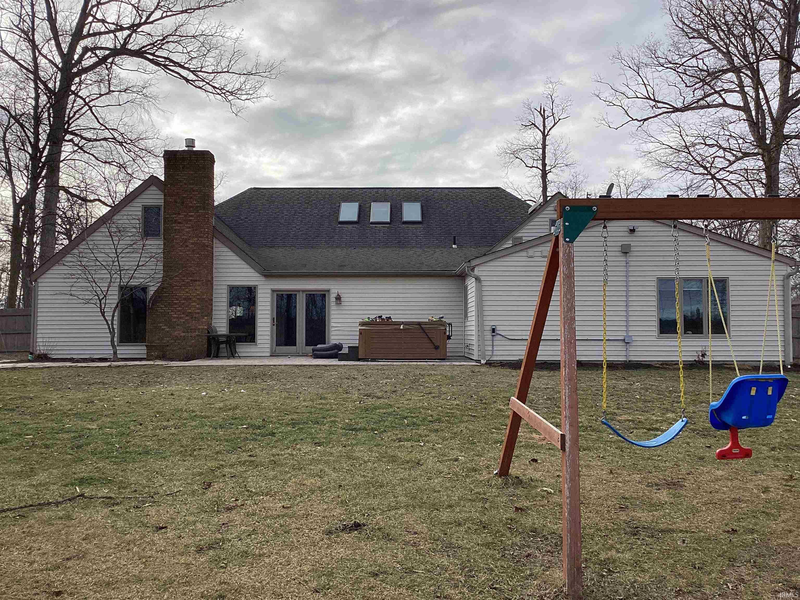 Back of property with a yard, a patio area, a chimney, a playground, and a hot tub