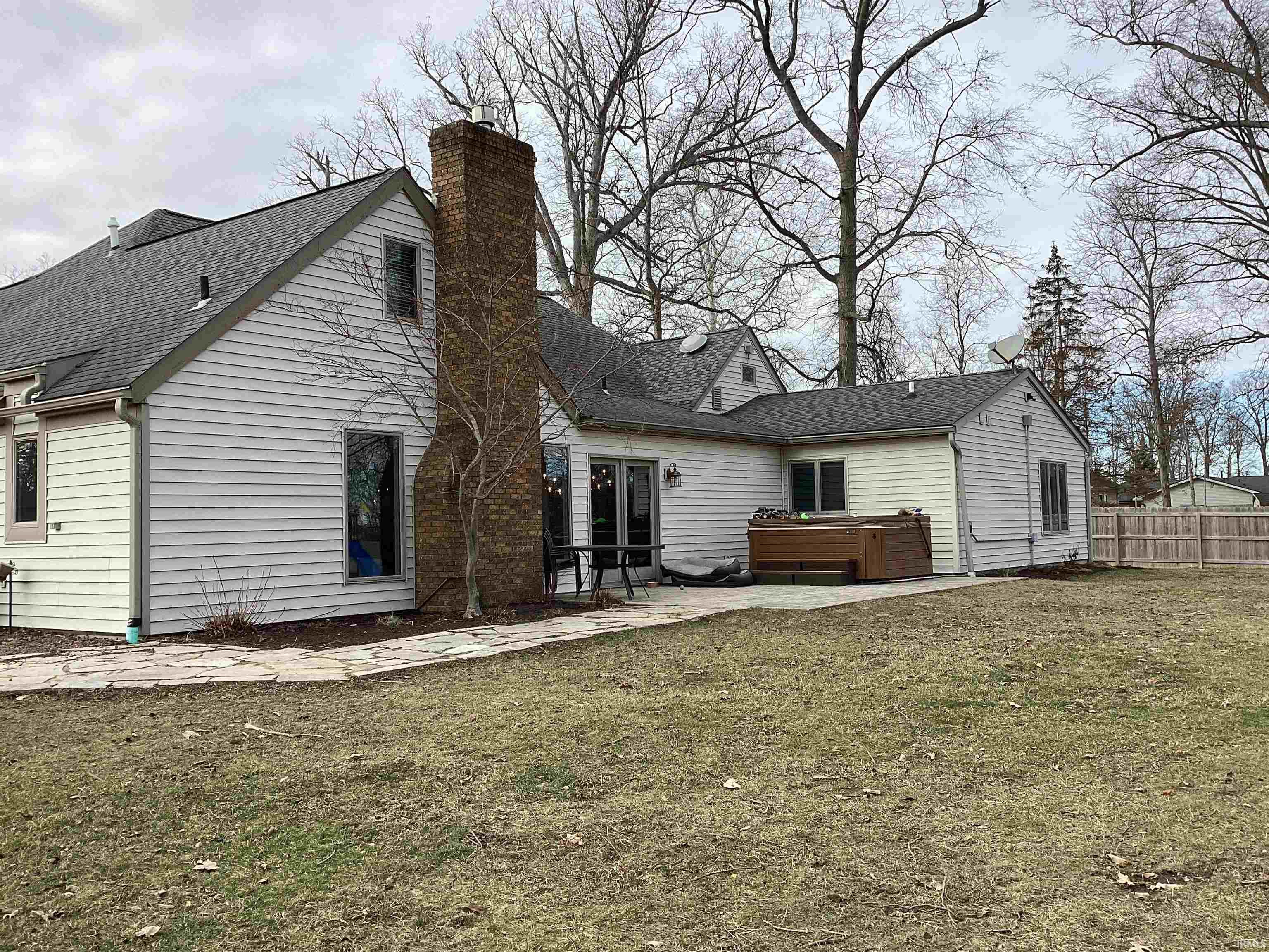 Rear view of property with a hot tub, roof with shingles, a chimney, and a patio area
