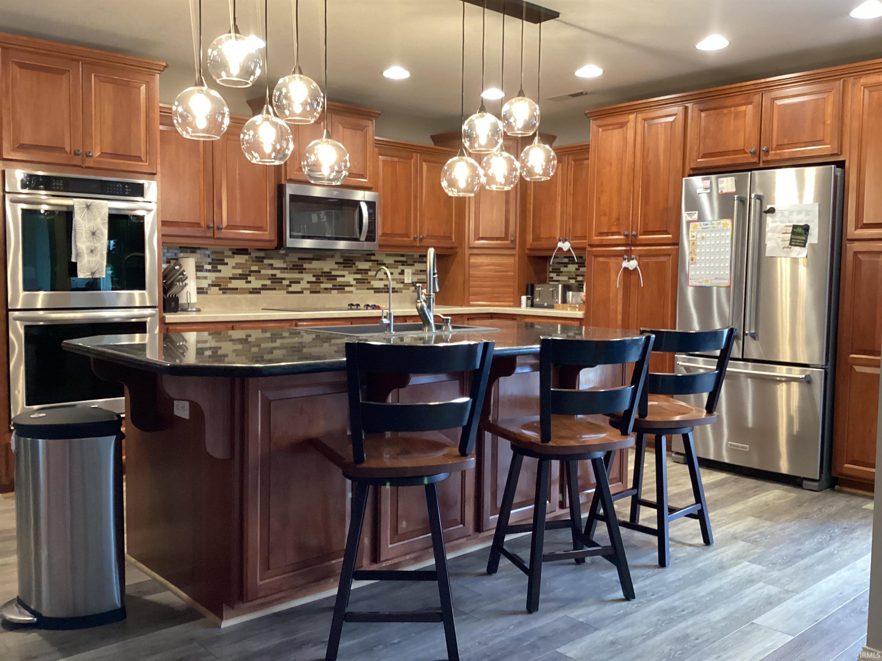 Kitchen featuring stainless steel appliances, wood finish cabinetry, backsplash, a breakfast bar, and decorative light fixtures