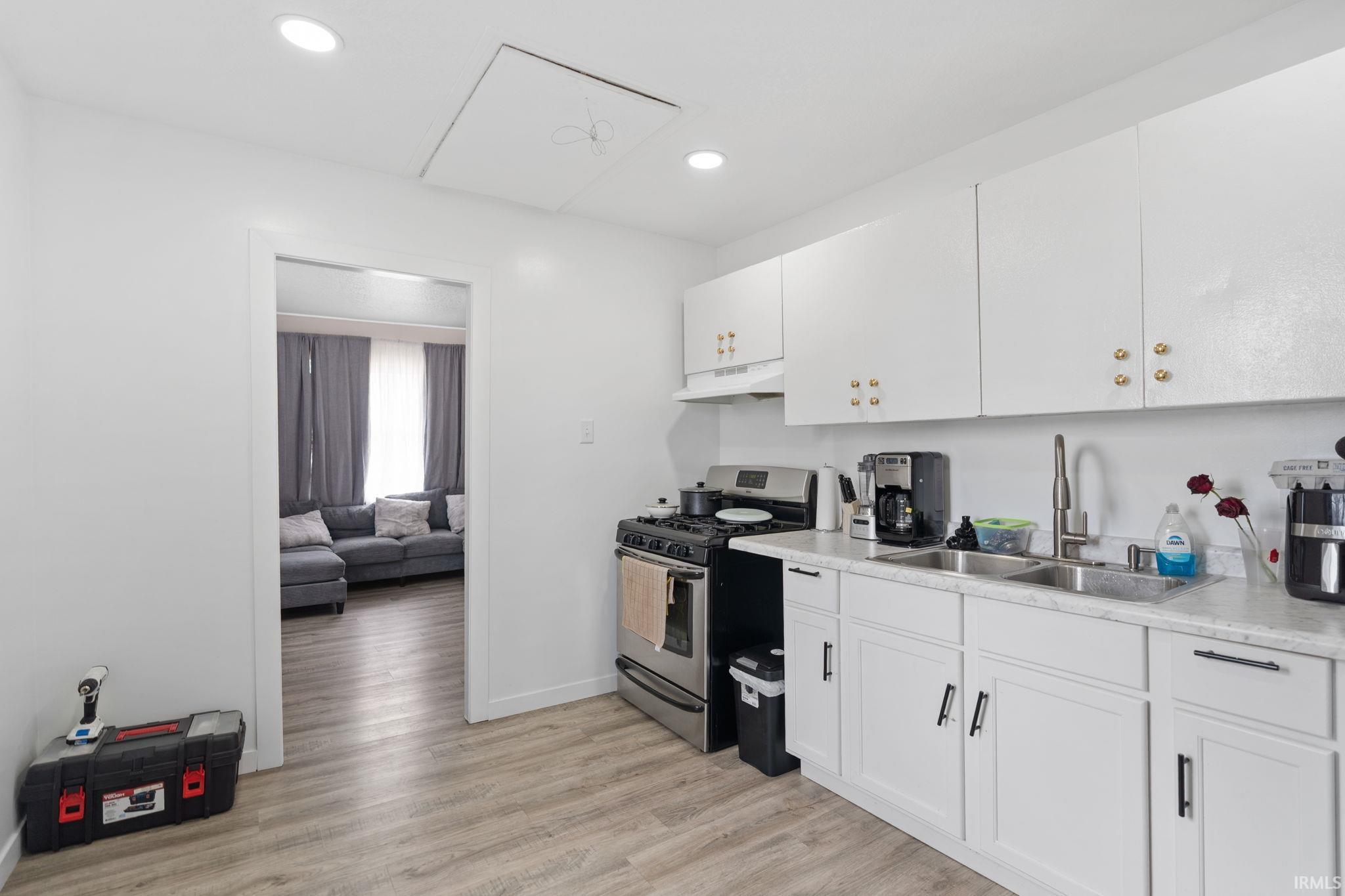 Kitchen with stainless steel gas range oven, light countertops, white cabinetry, light wood-type flooring, and recessed lighting