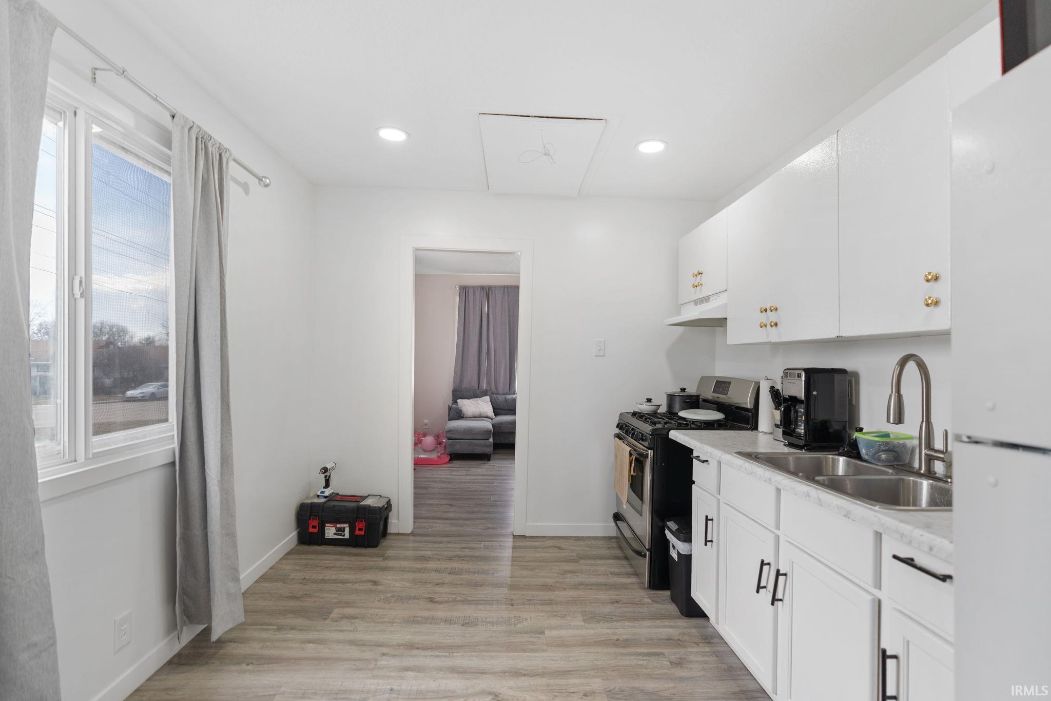 Kitchen with freestanding refrigerator, light countertops, stainless steel gas range oven, light wood-style floors, and white cabinetry