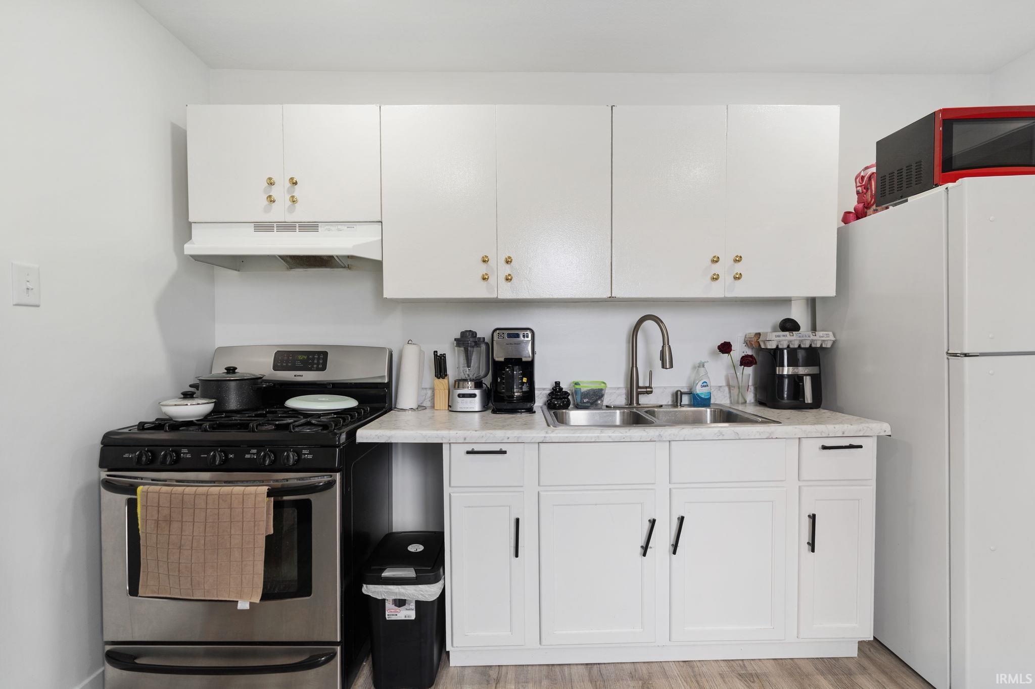 Kitchen with gas range, freestanding refrigerator, light countertops, white cabinets, and light wood-style floors