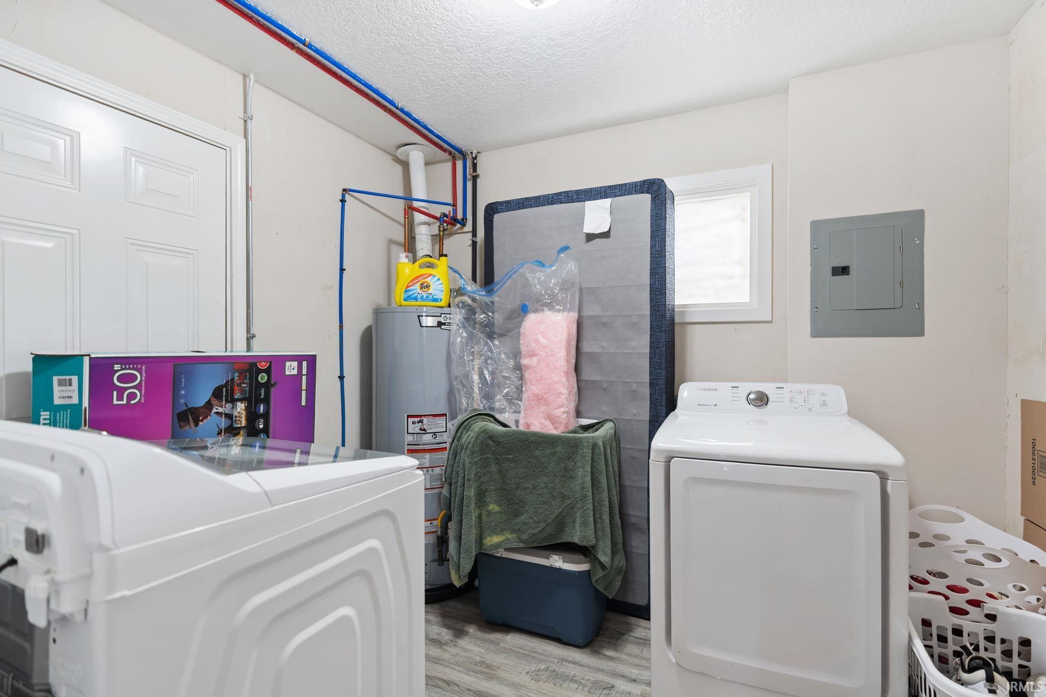 Laundry room featuring washer / dryer, a textured ceiling, electric panel, light wood finished floors, and water heater