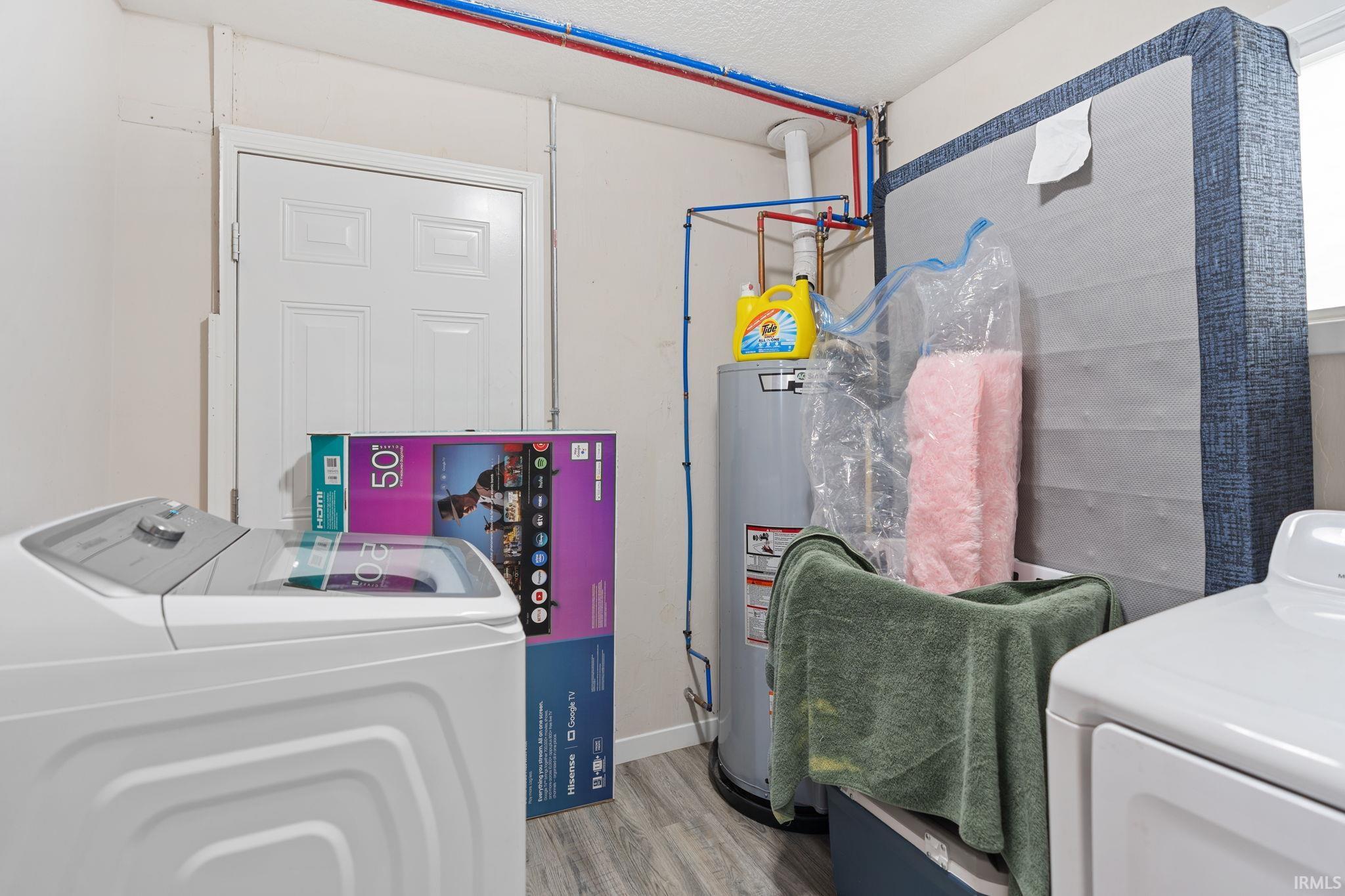Laundry room featuring wood finished floors, water heater, separate washer and dryer, and a textured ceiling