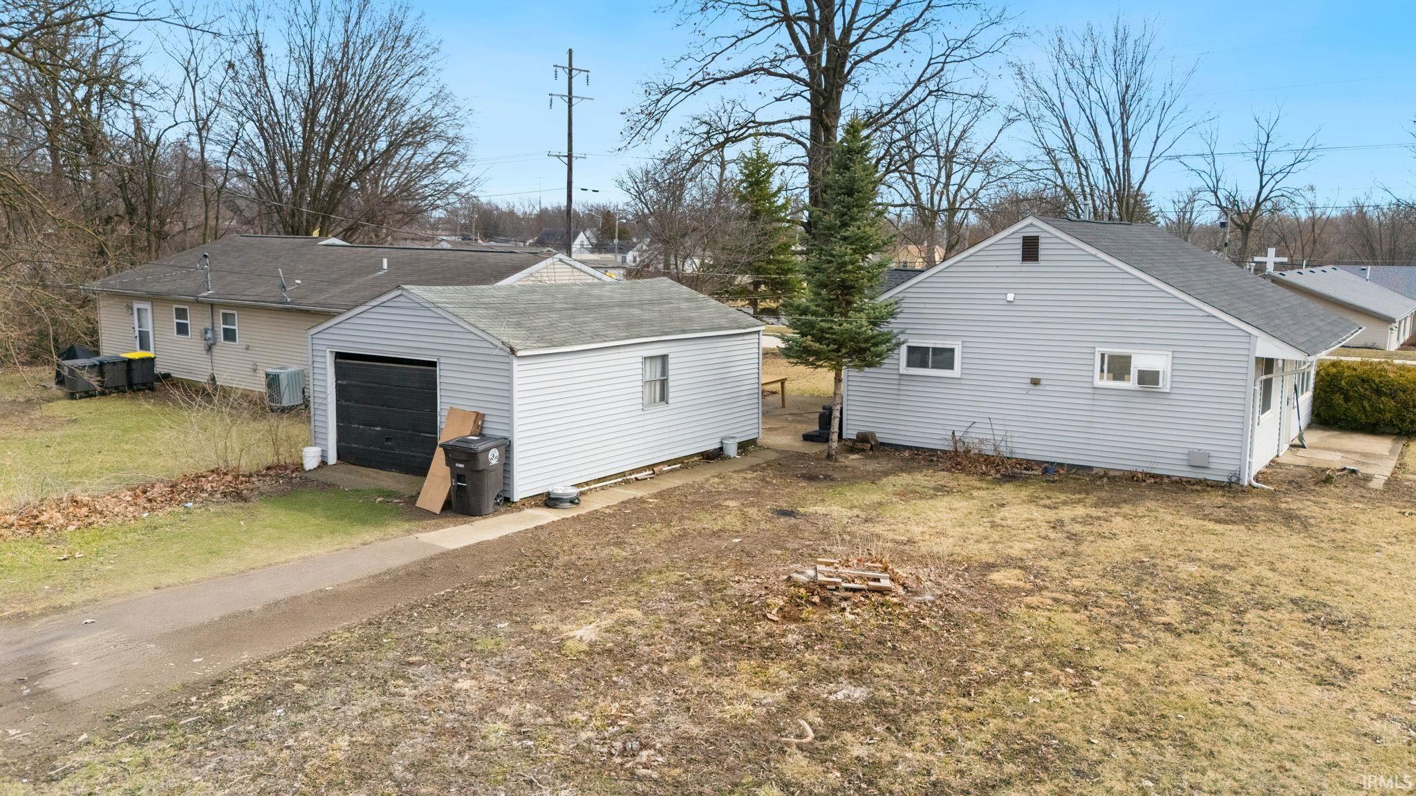 Rear view of property with a garage, a shingled roof, an outbuilding, and a lawn