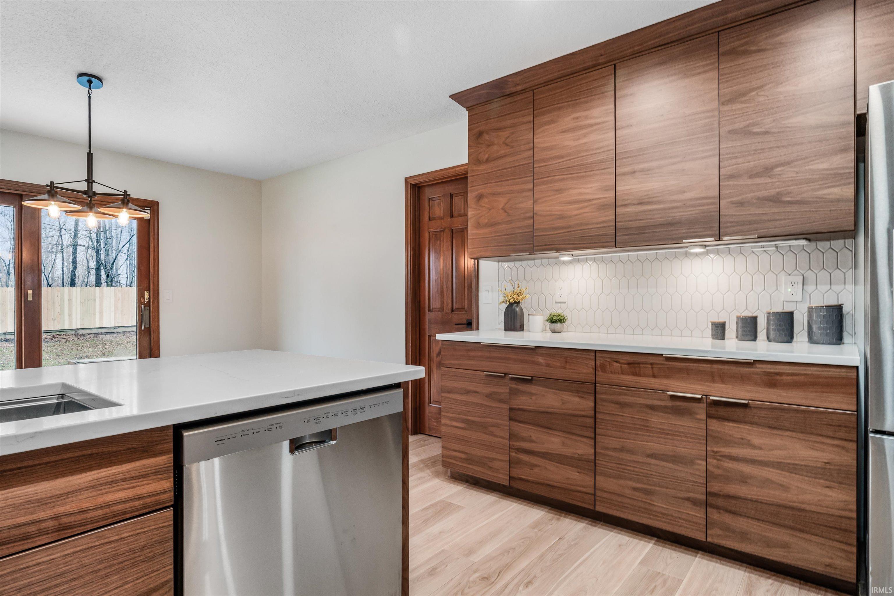 Kitchen featuring stainless steel appliances, decorative backsplash, light wood-style floors, light stone counters, and hanging light fixtures