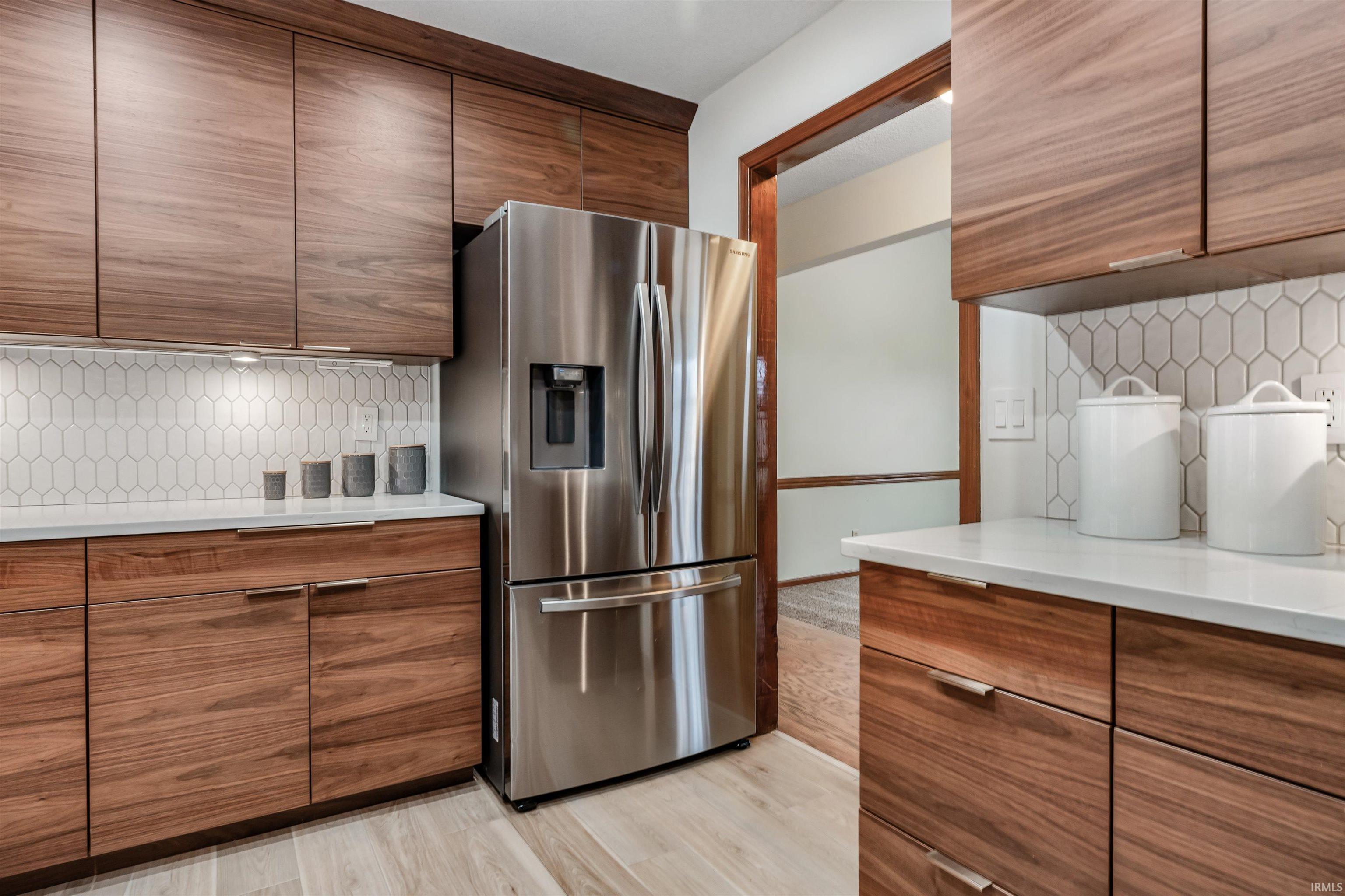 Kitchen with decorative backsplash, stainless steel refrigerator with ice dispenser, modern cabinets, and light wood-type flooring