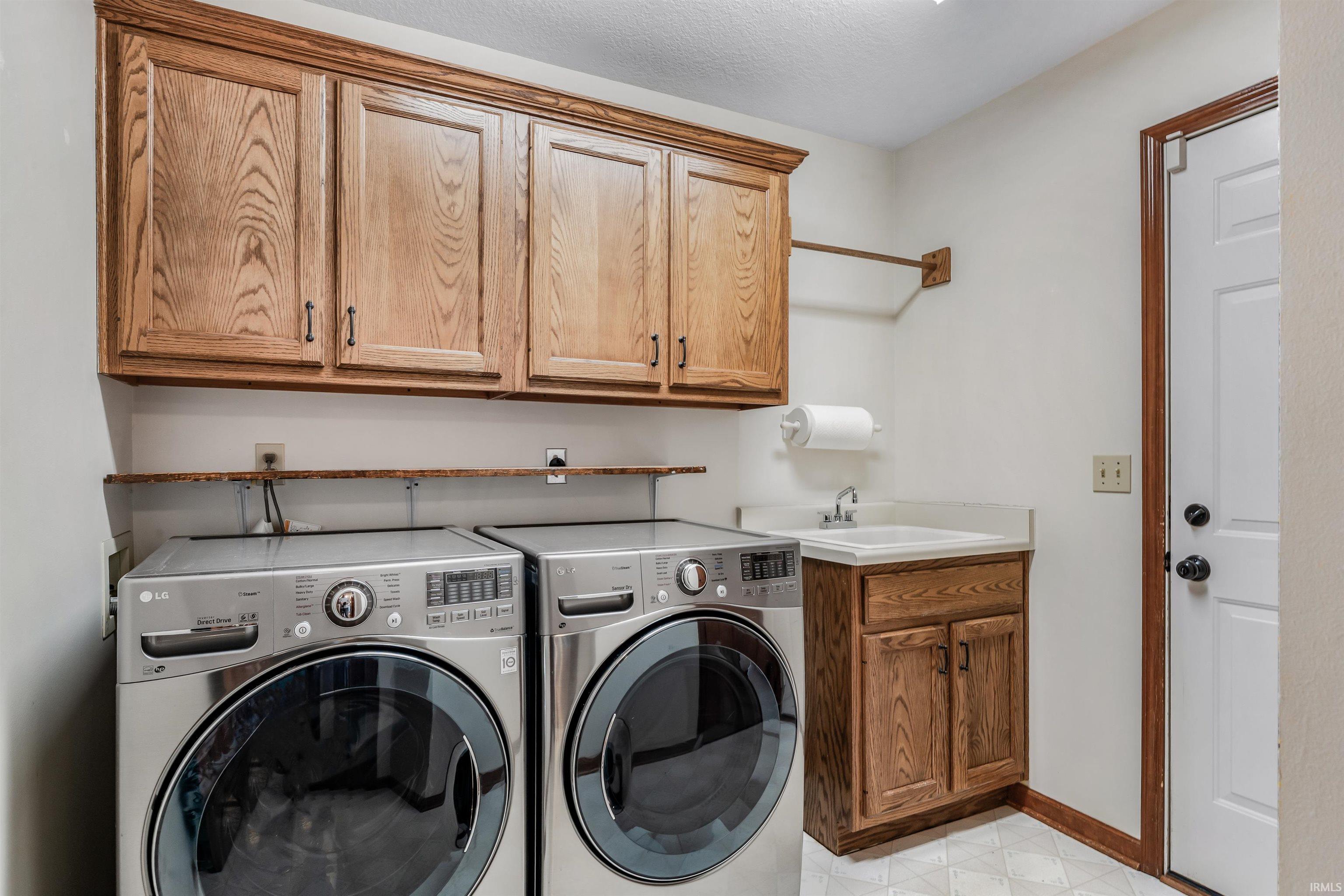 Laundry room featuring washer and clothes dryer, cabinet space, light floors, and a textured ceiling