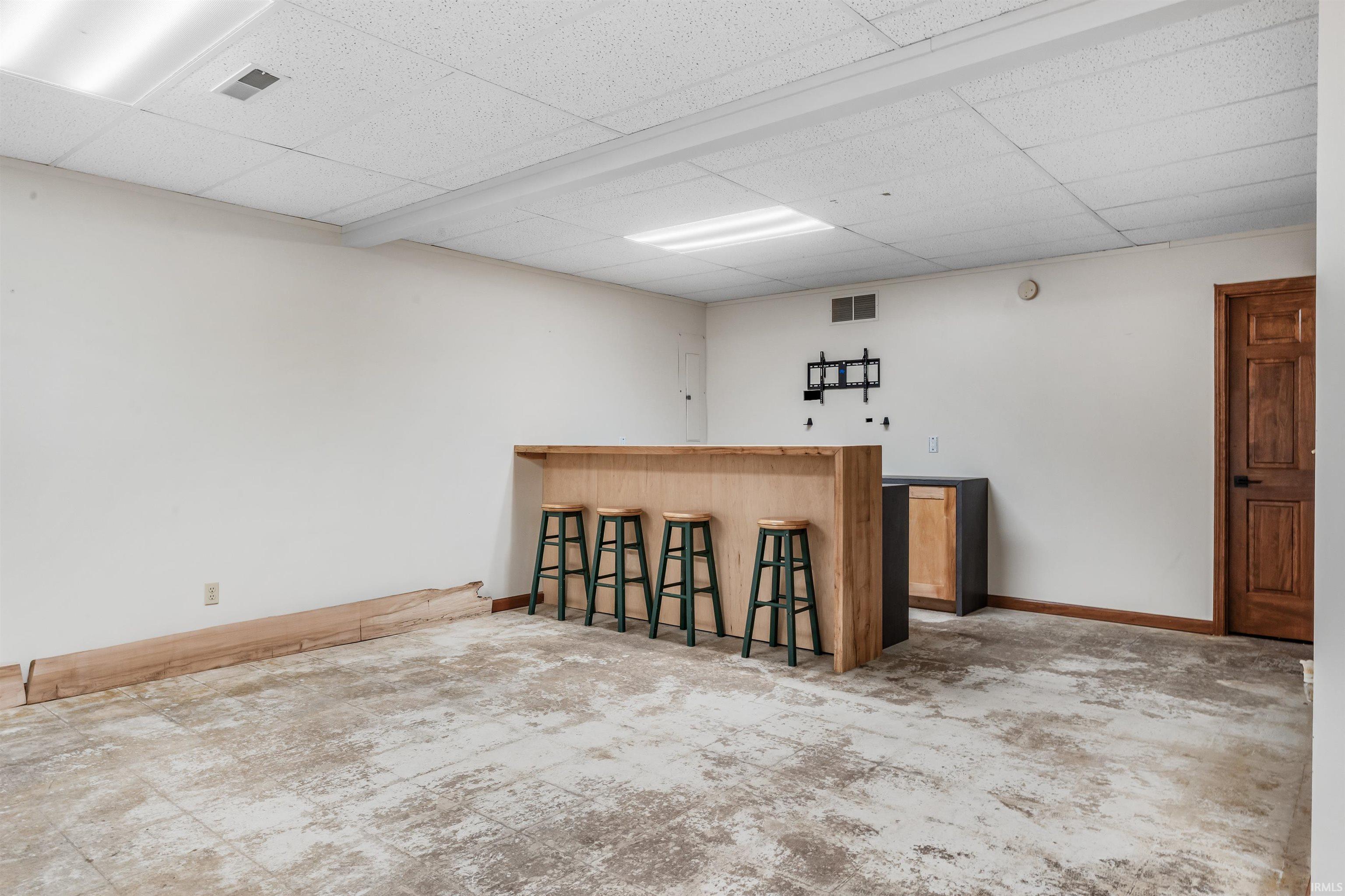 Indoor dry bar with a drop ceiling and dark countertops