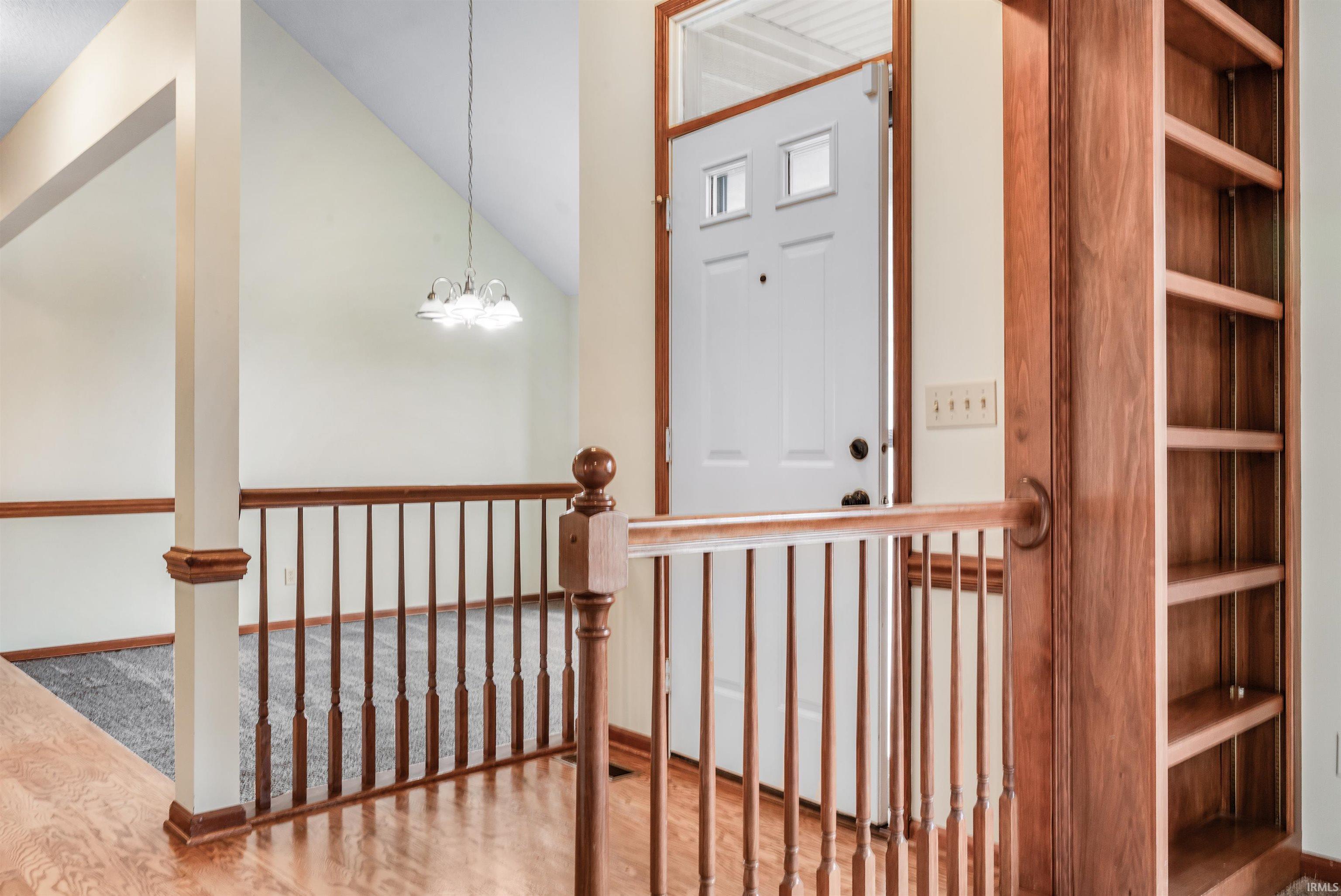 Foyer with wood finished floors, vaulted ceiling, and a chandelier
