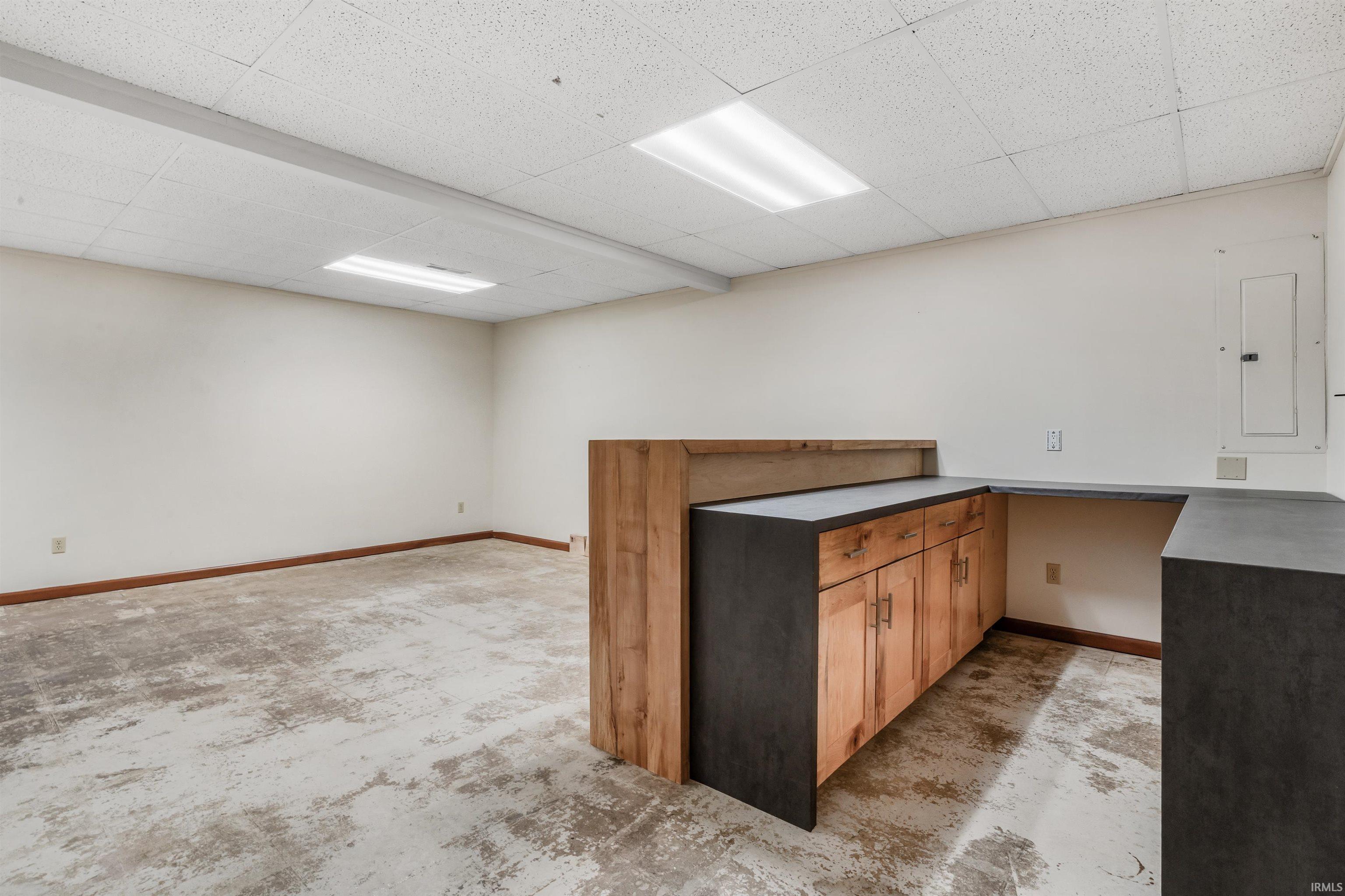 Kitchen featuring electric panel, wood finish cabinets, dark countertops, a peninsula, and a paneled ceiling