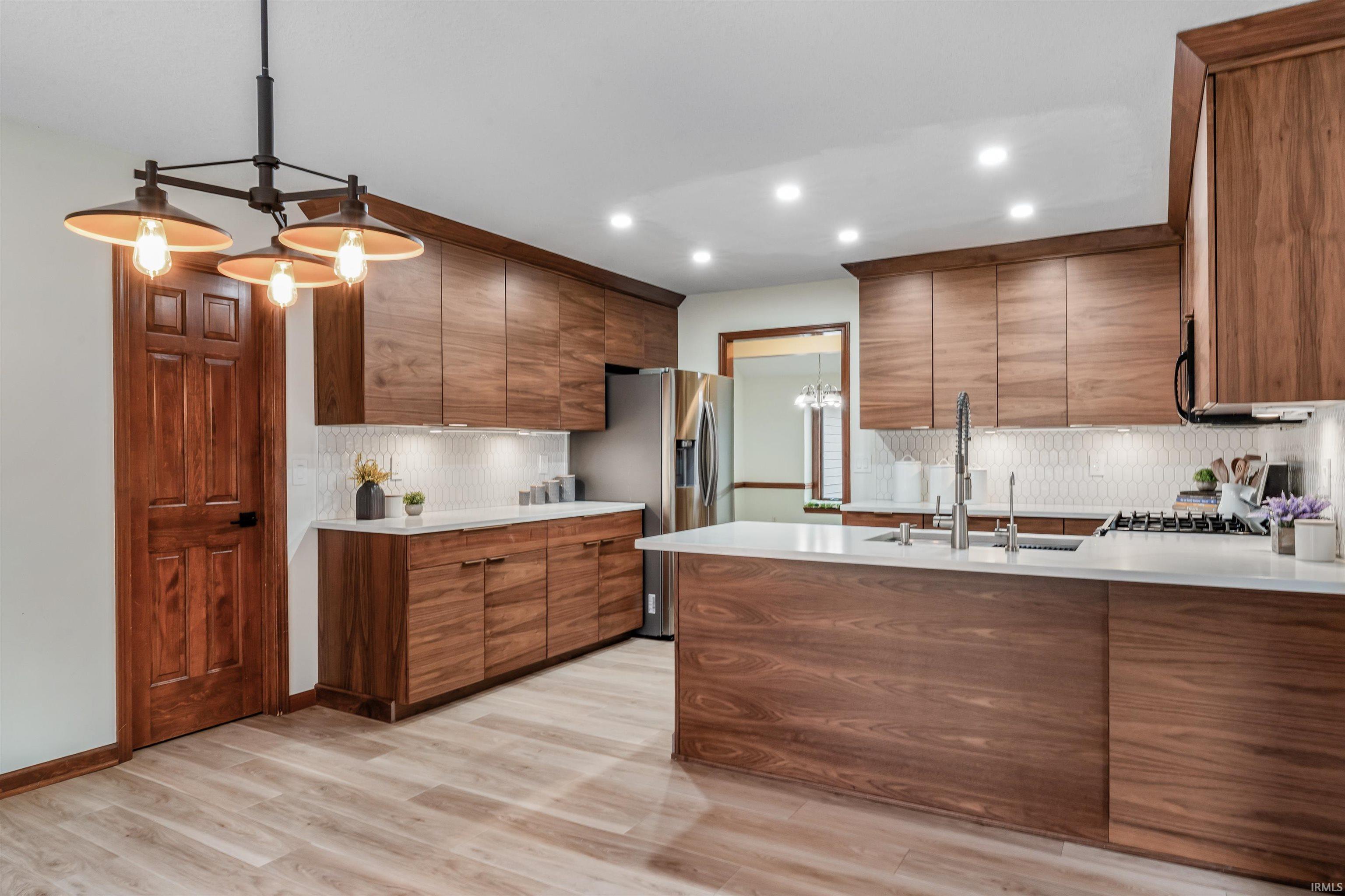 Kitchen featuring suspended lighting, a peninsula, tasteful backsplash, stainless steel appliances, and wood finish cabinets