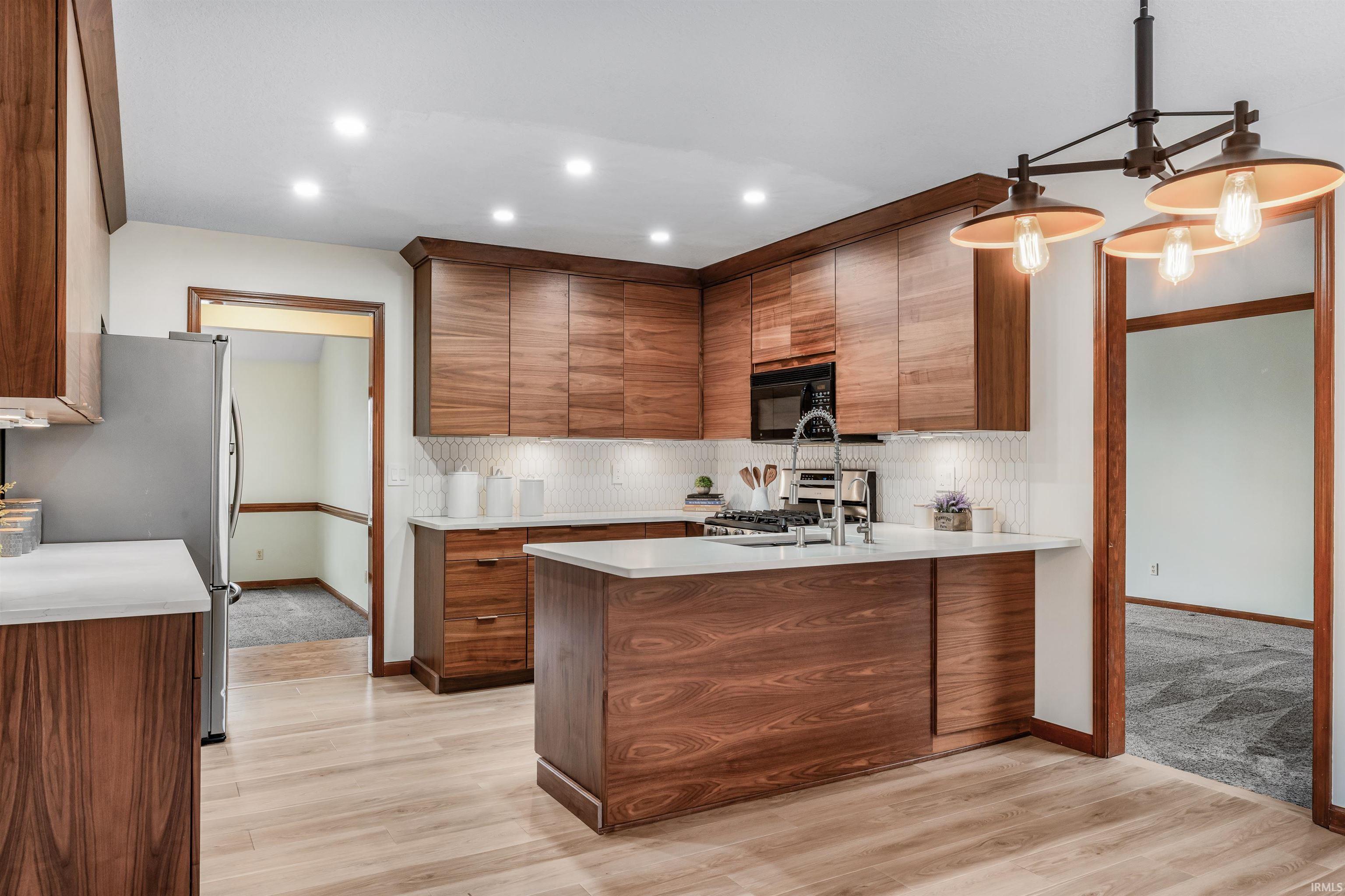 Kitchen with stainless steel appliances, a peninsula, light wood-style floors, wood finish cabinetry, and light stone counters