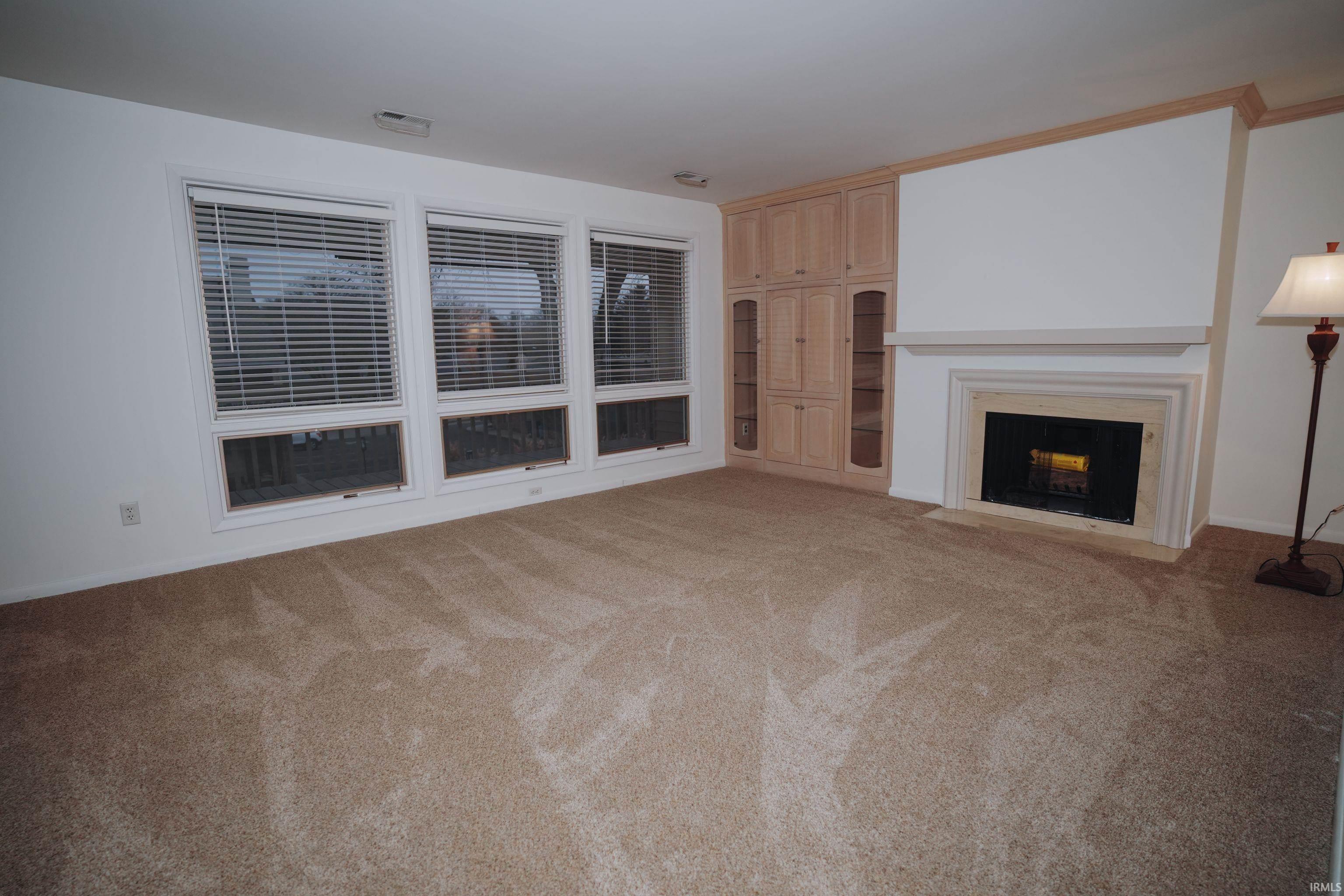 Unfurnished living room with a fireplace with flush hearth and light carpet