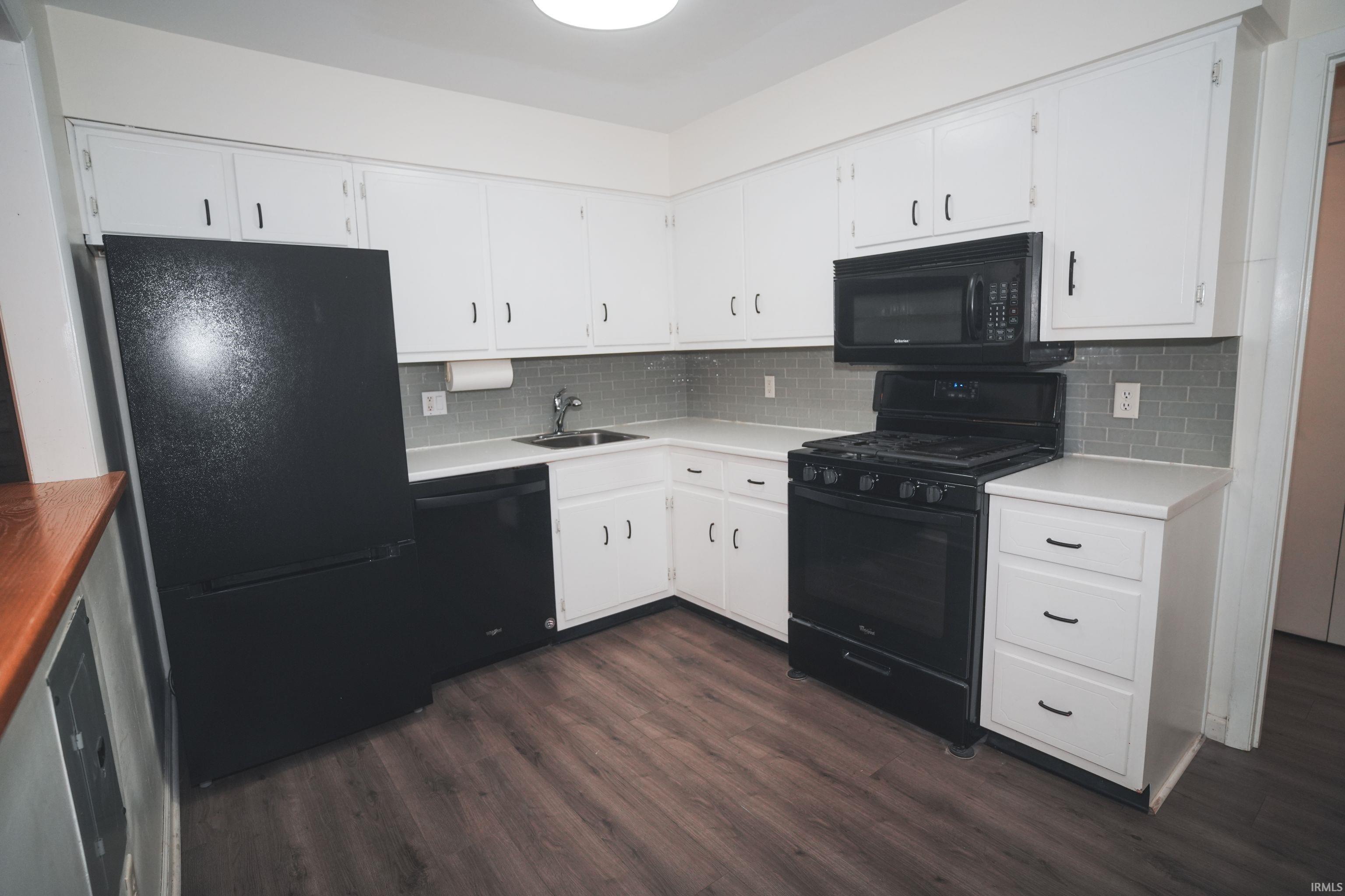 Kitchen with black appliances, white cabinets, dark wood-style flooring, and decorative backsplash