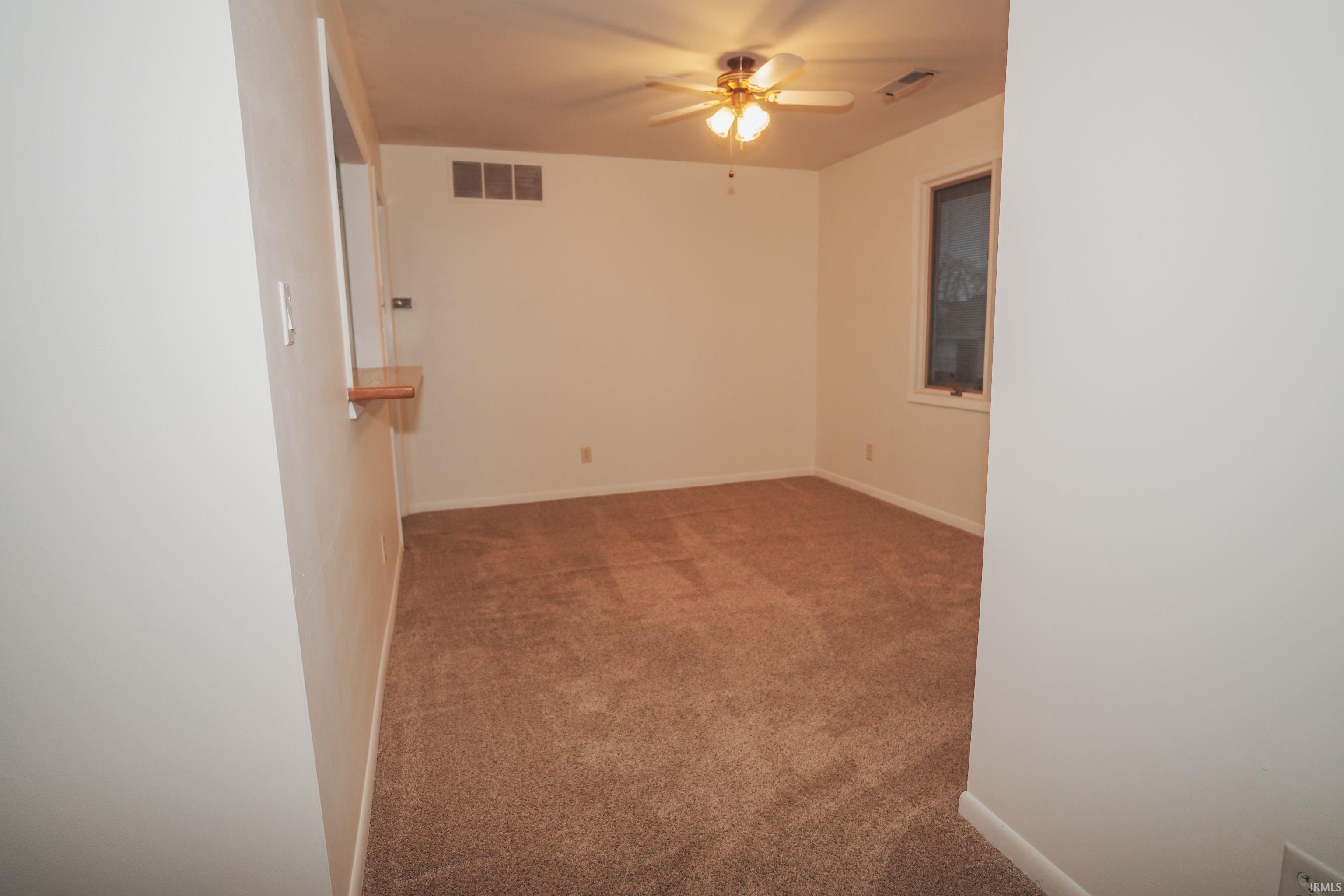 Carpeted spare room featuring ceiling fan and baseboards