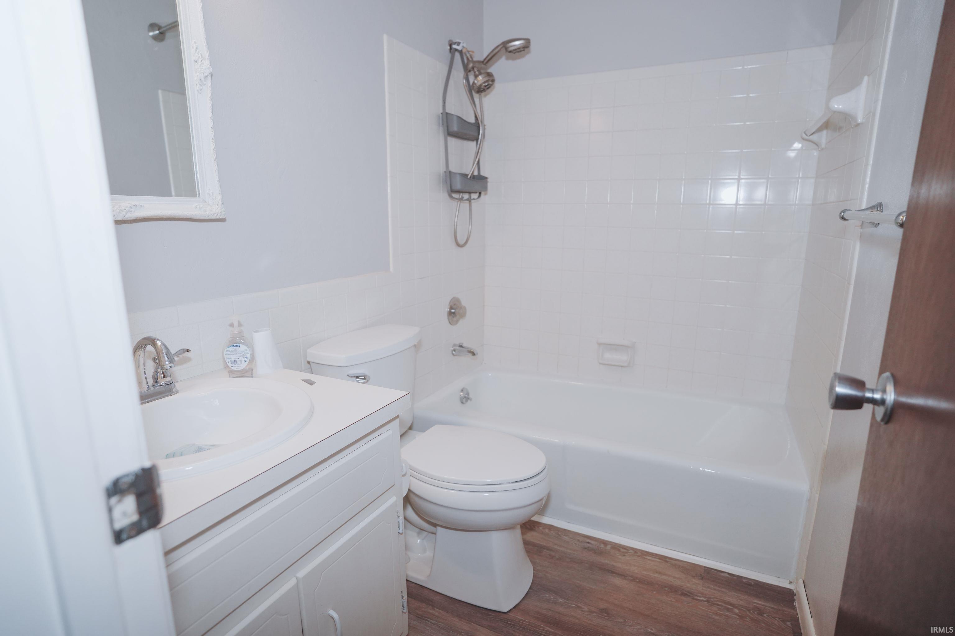 Full bathroom featuring vanity, bathtub / shower combination, dark wood finished floors, tile walls, and wainscoting