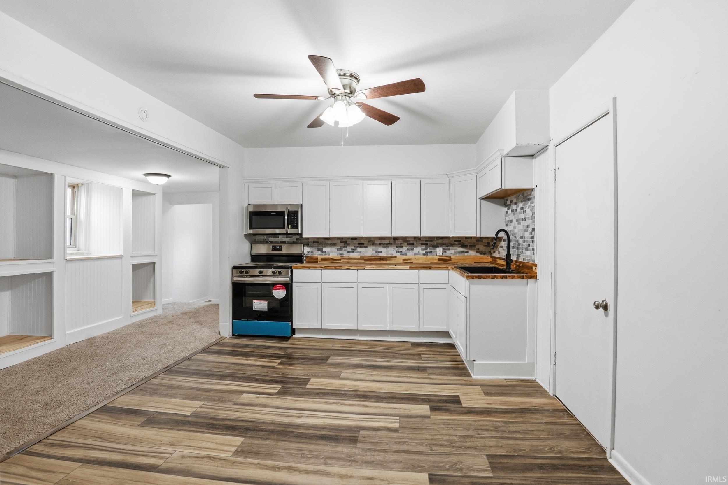 Kitchen with wood counters, tasteful backsplash, stainless steel appliances, white cabinets, and a ceiling fan