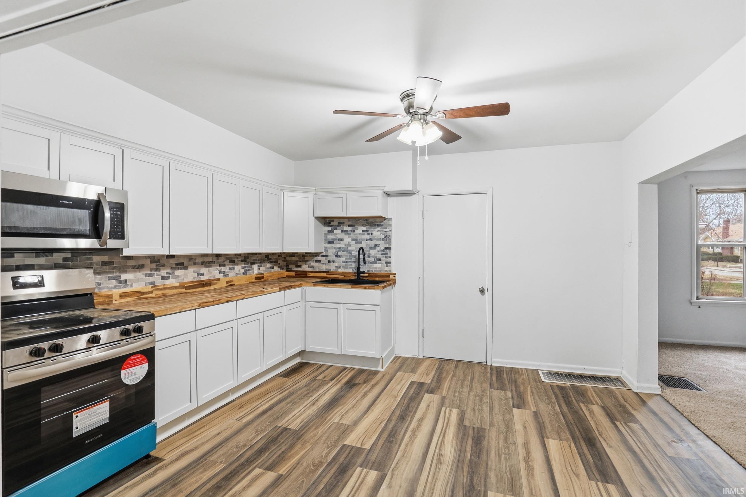 Kitchen with wooden counters, stainless steel appliances, white cabinetry, and tasteful backsplash