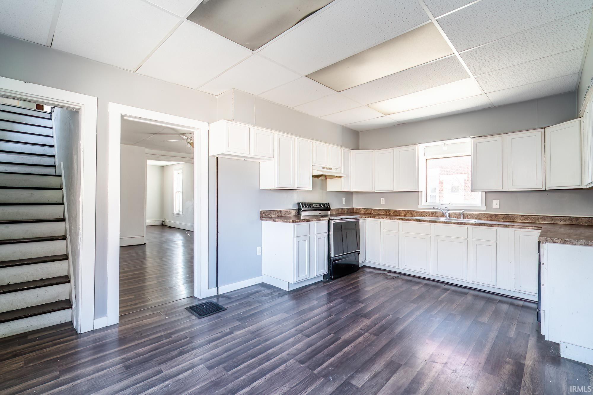 Kitchen with white cabinets, electric range, a drop ceiling, dark wood-type flooring, and dark countertops