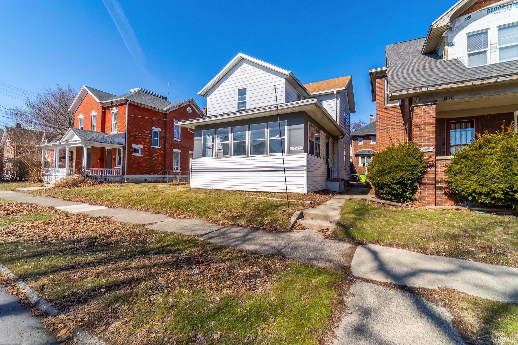View of front facade featuring covered porch, a front lawn, a shingled roof, and brick siding