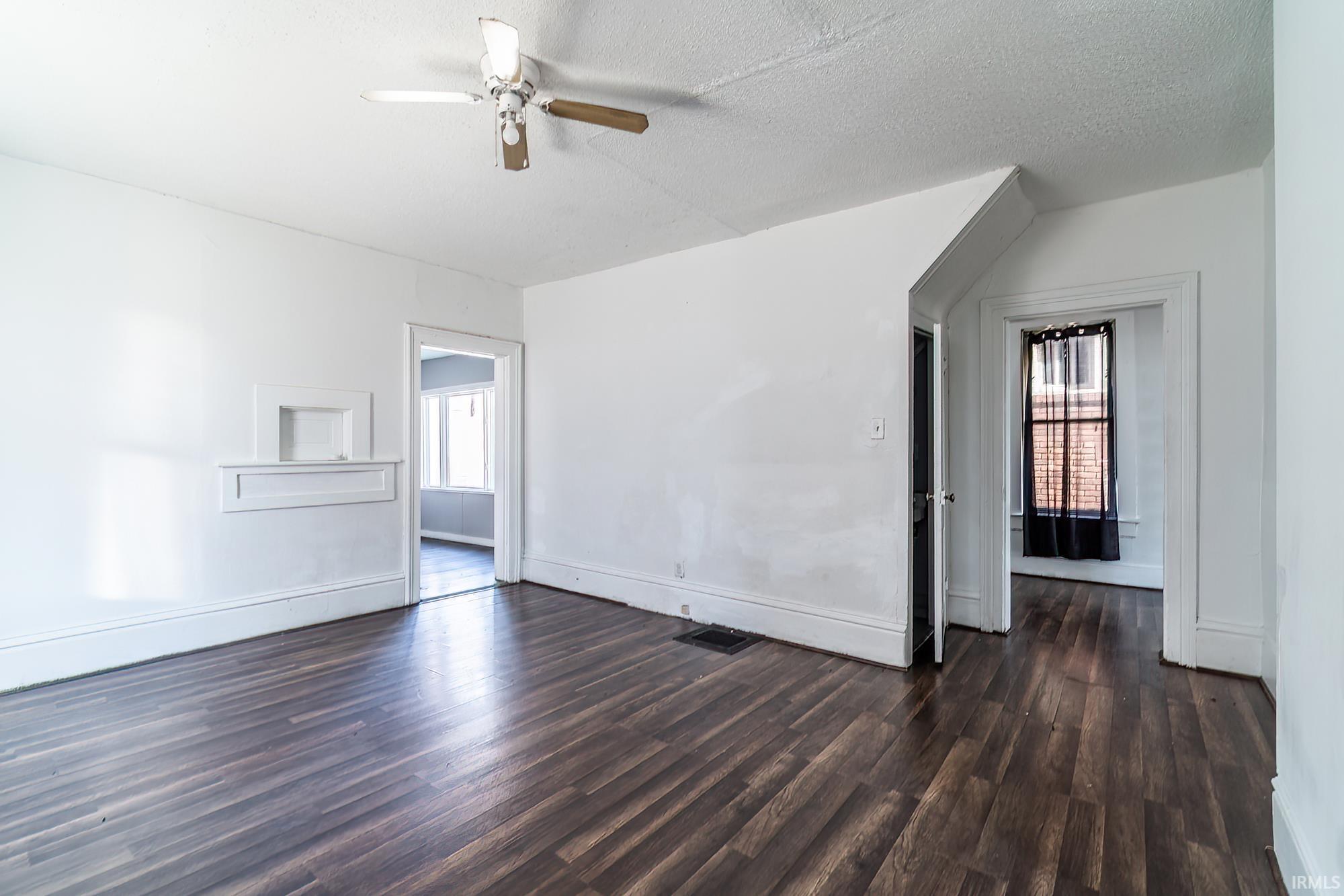Empty room with a textured ceiling, dark wood-style floors, and ceiling fan