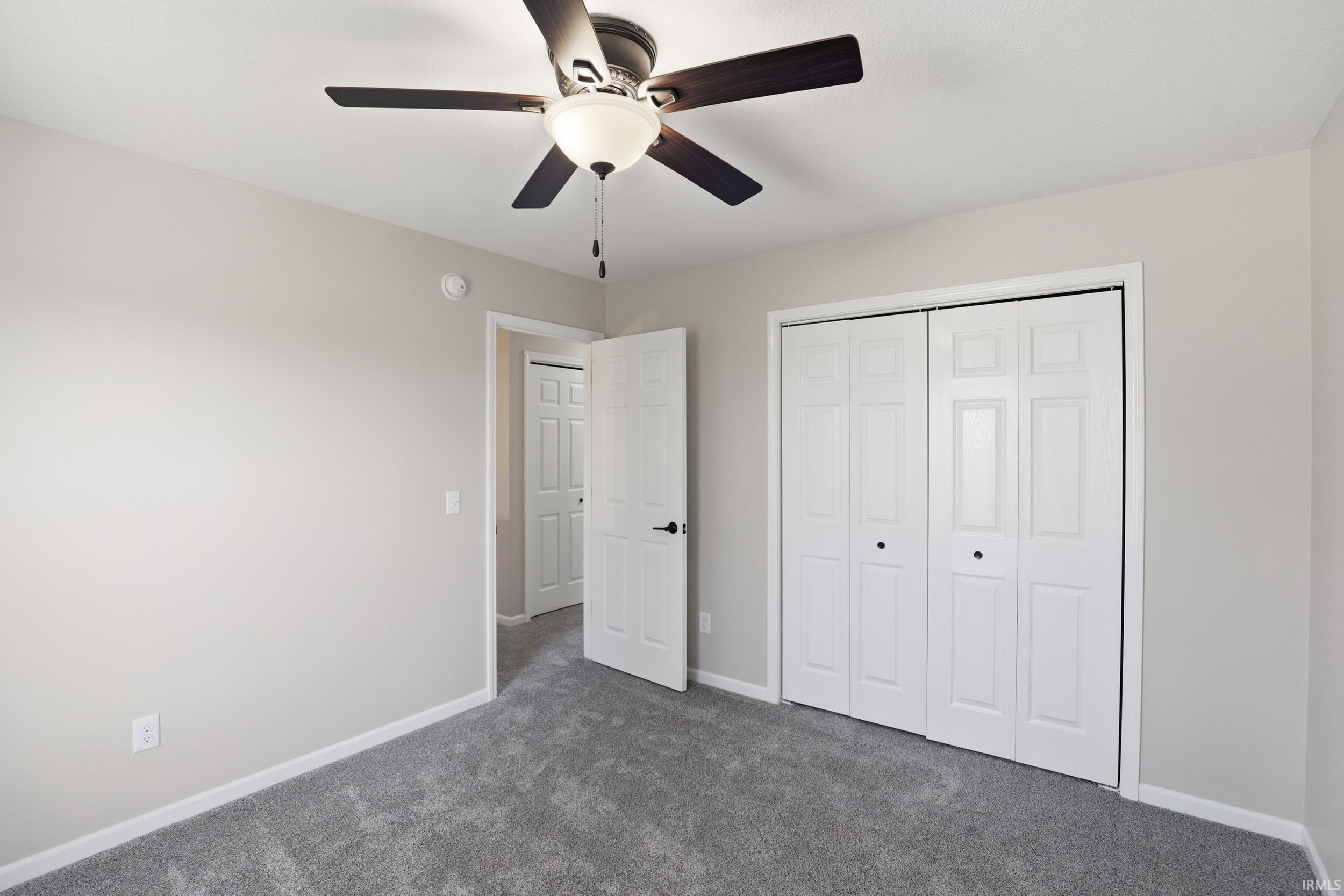 Unfurnished bedroom featuring dark colored carpet, a closet, and a ceiling fan